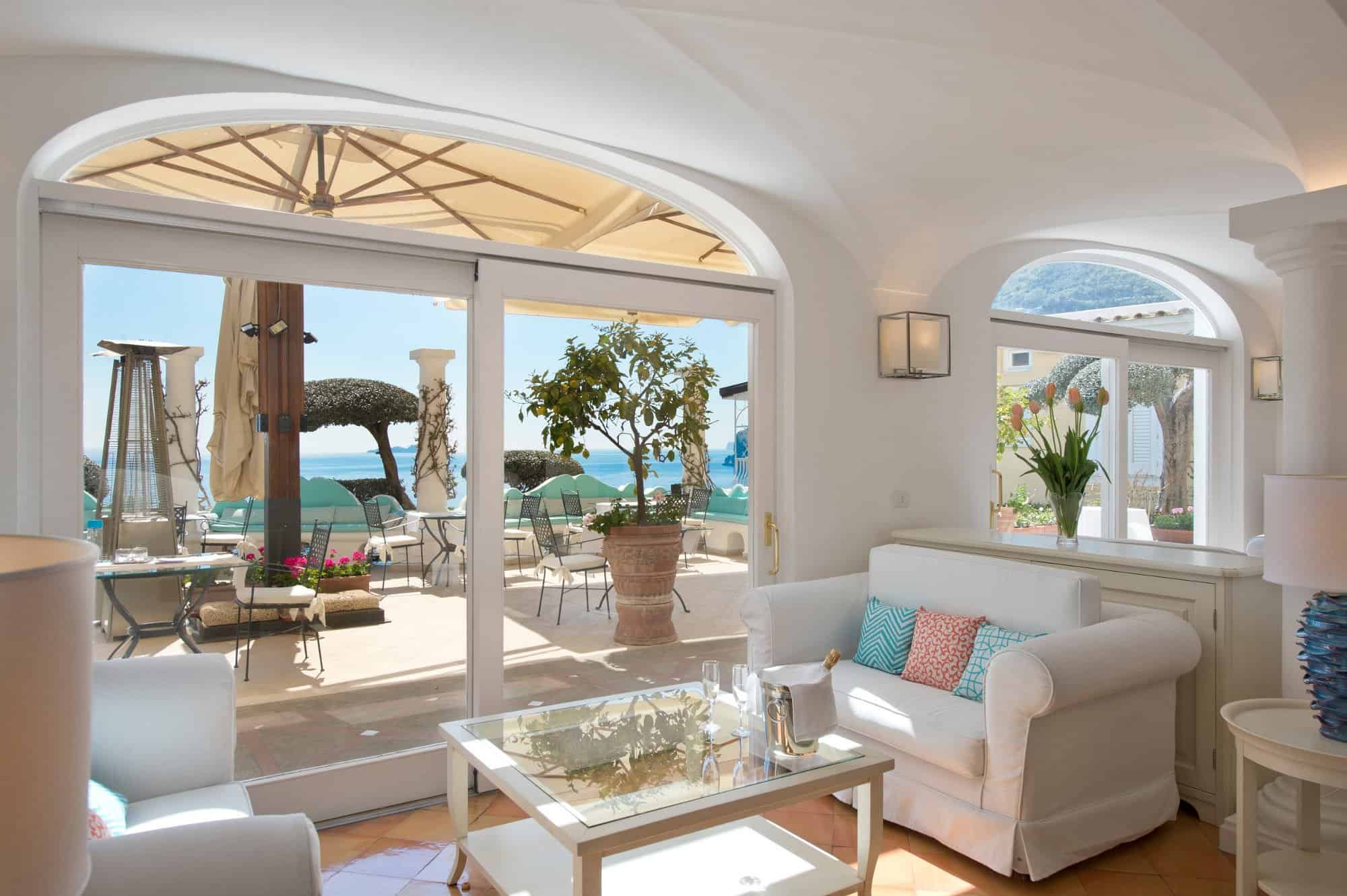 Bright white hotel suite in Positano with arched doorways opening onto a sea-view terrace, lemon tree and Amalfi Coast views — luxury European summer vacations