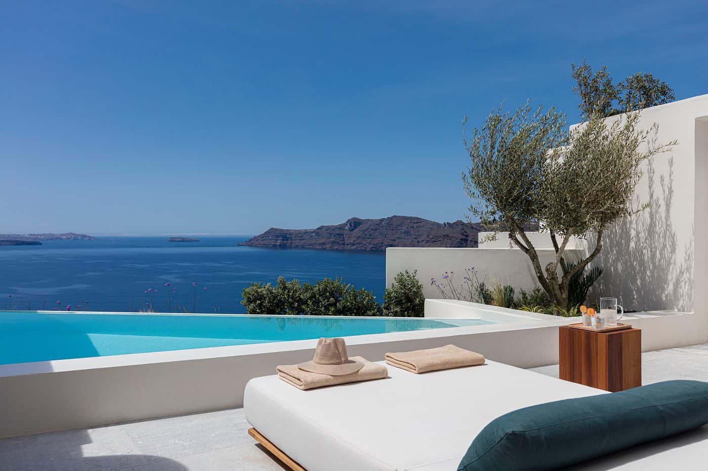 Private infinity pool villa in Santorini overlooking the caldera and Aegean Sea, with sunlounger and olive tree — best hotels in Santorini Greece