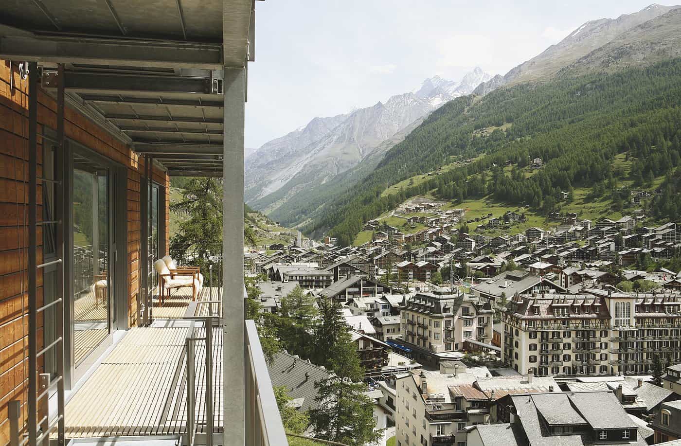 Hotel balcony overlooking Zermatt village and Swiss Alps in summer, with wooden chalet architecture and mountain views perfect for European summer vacations