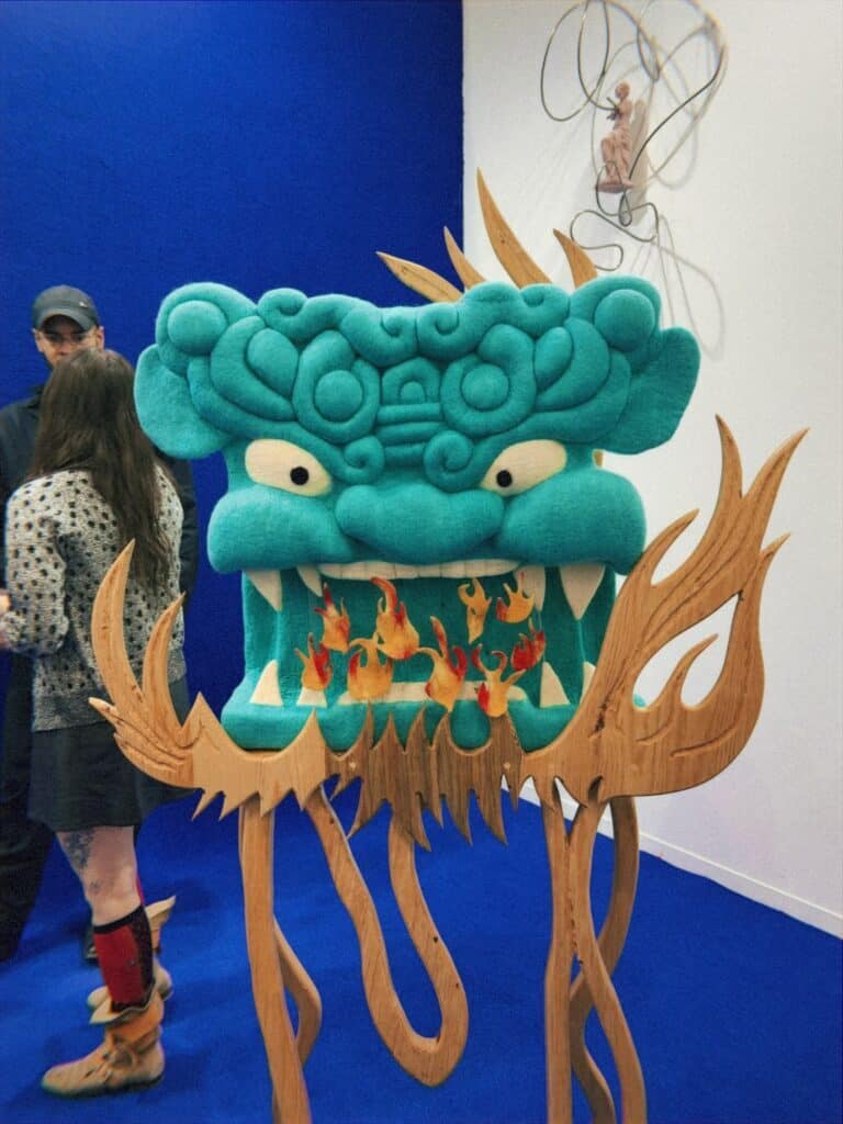 Turquoise monster sculpture with wooden flames at CDMX art fair exhibition space
