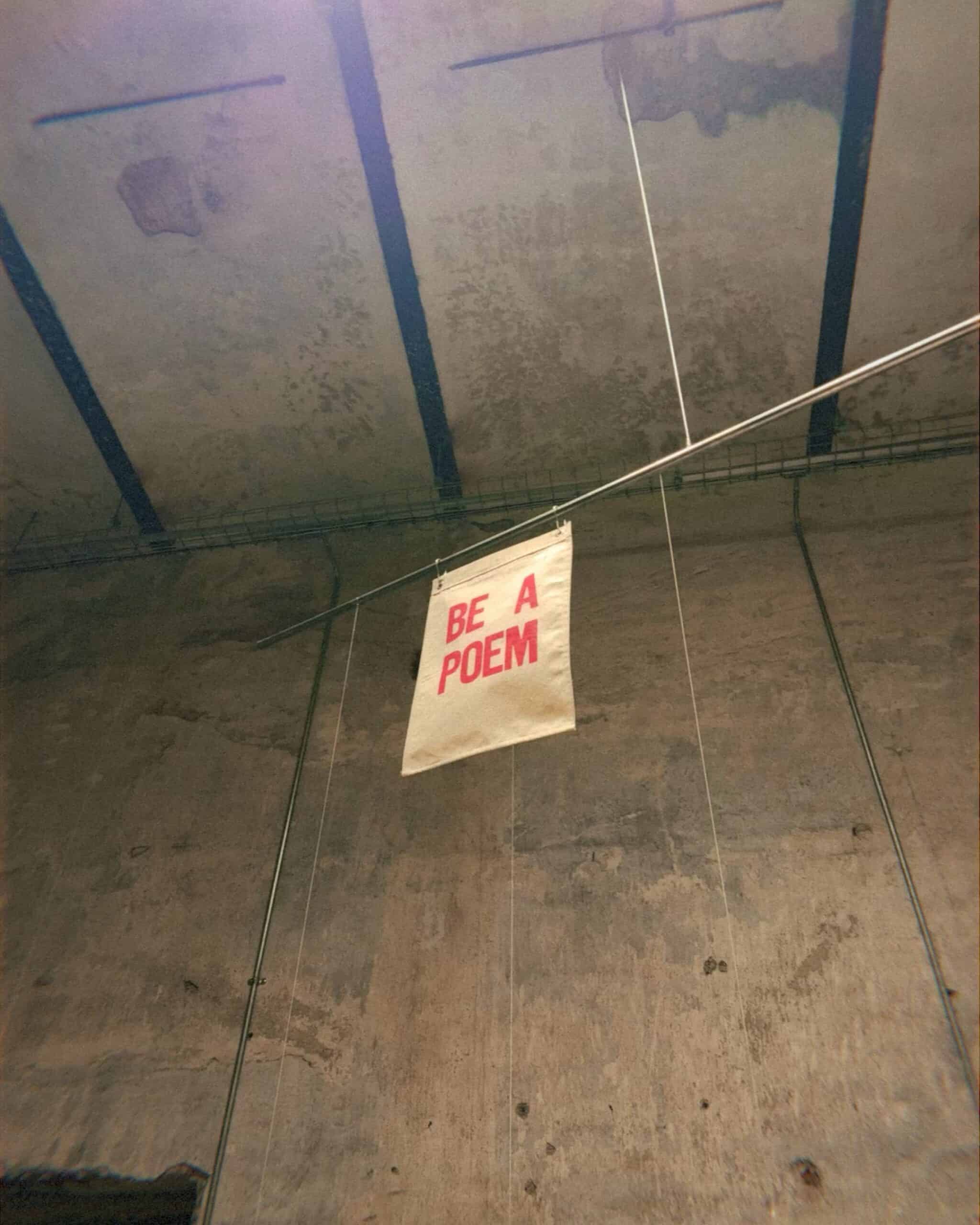 Be A Poem banner hanging from ceiling at contemporary art Mexico City warehouse exhibition Salon Acme