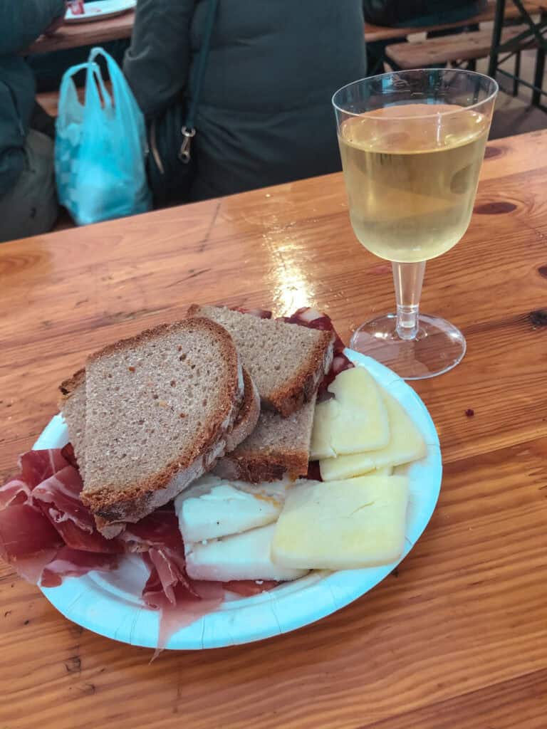 Portuguese charcuterie plate with cured ham, local cheese and crusty bread served with a glass of white wine at a Lisbon food market — what to eat in Lisbon Portugal