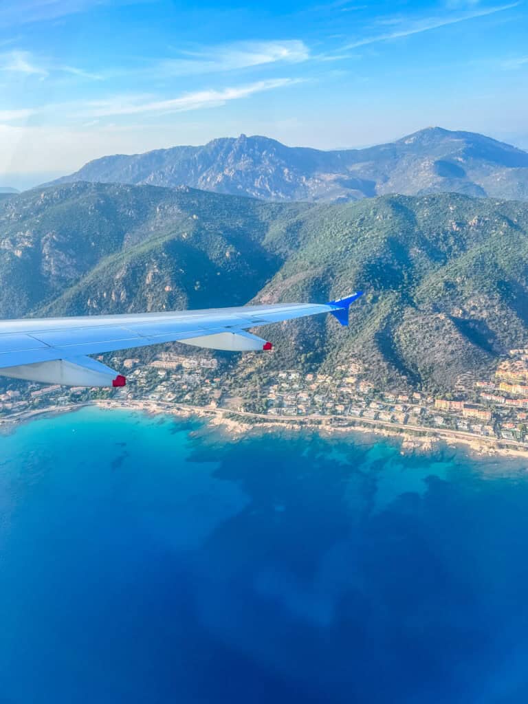 Aerial view of Corsica's turquoise coastline, mountain interior and coastal town from an Air Corsica plane window — European summer vacations flying to Corsica
