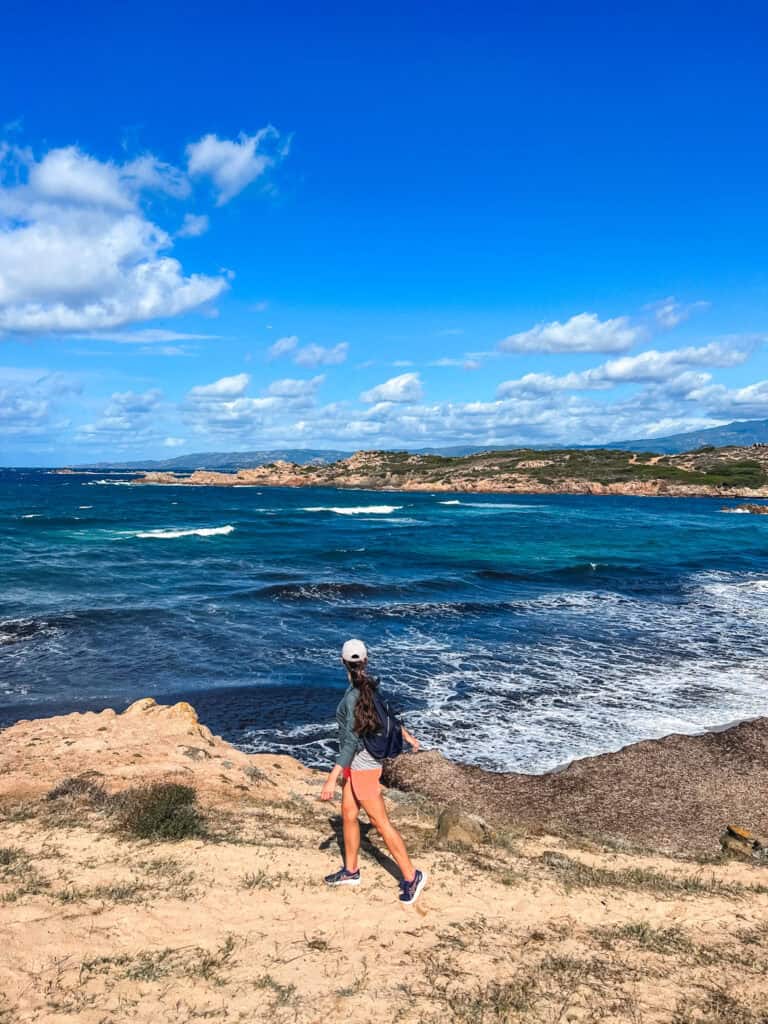 Woman hiking along the rugged coastline of northern Corsica with turquoise Mediterranean Sea and rocky headlands — things to do in Corsica France
