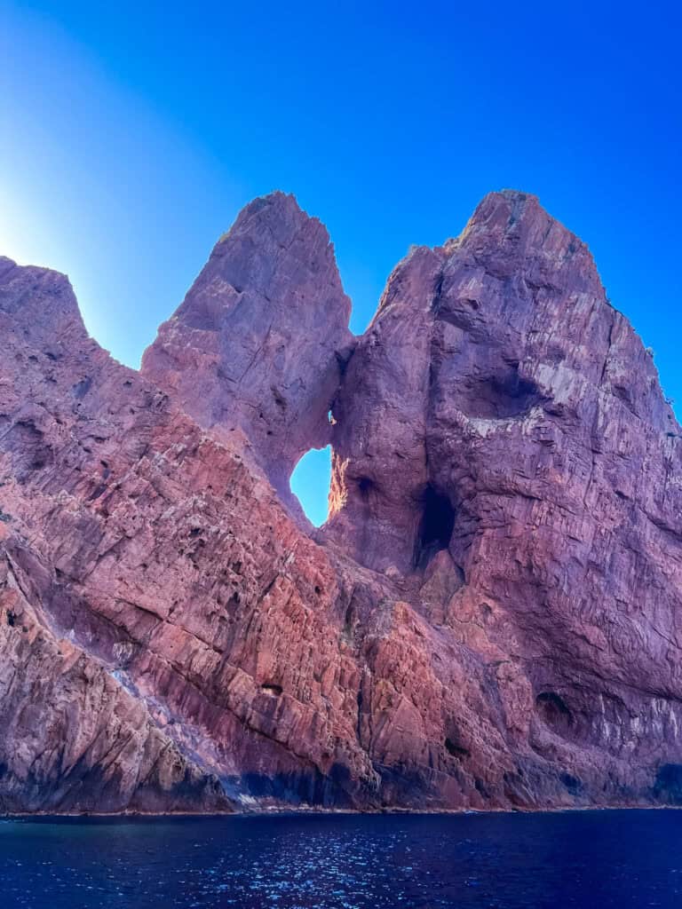 Burnt orange granite cliffs and sea caves of the Calanques de Piana viewed from the water, Corsica — European summer vacations Corsica boat tour