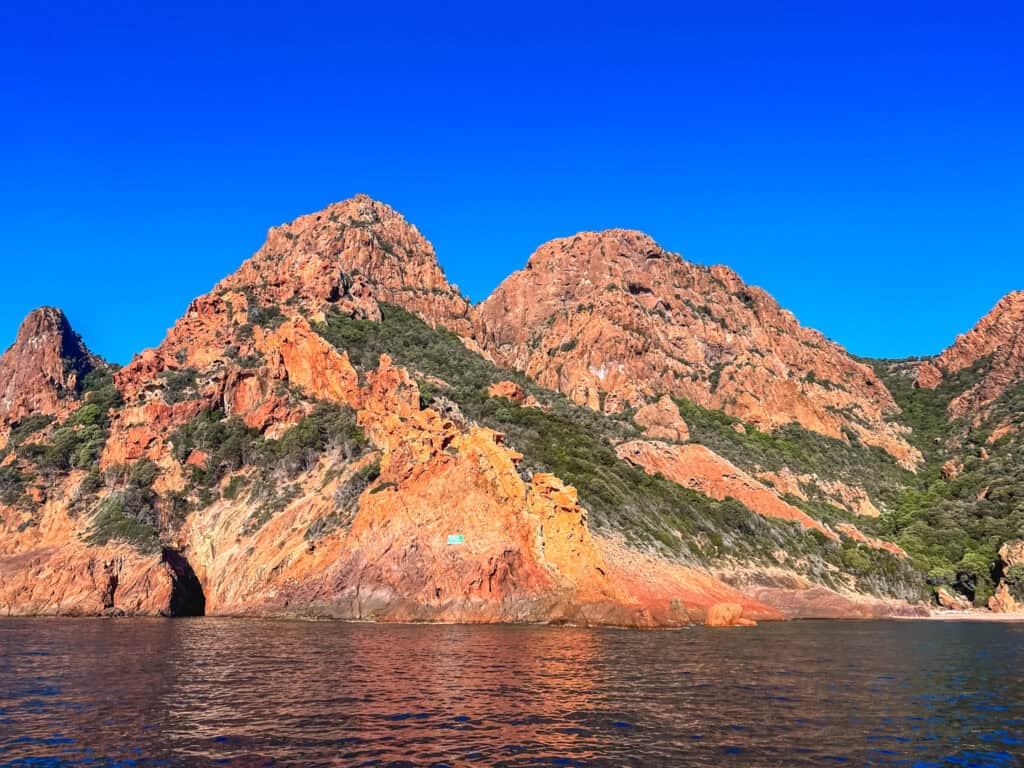 Dramatic red granite rock arch in the Calanques de Piana seen from a boat tour, Corsica — European summer vacations boat trips Corsica
