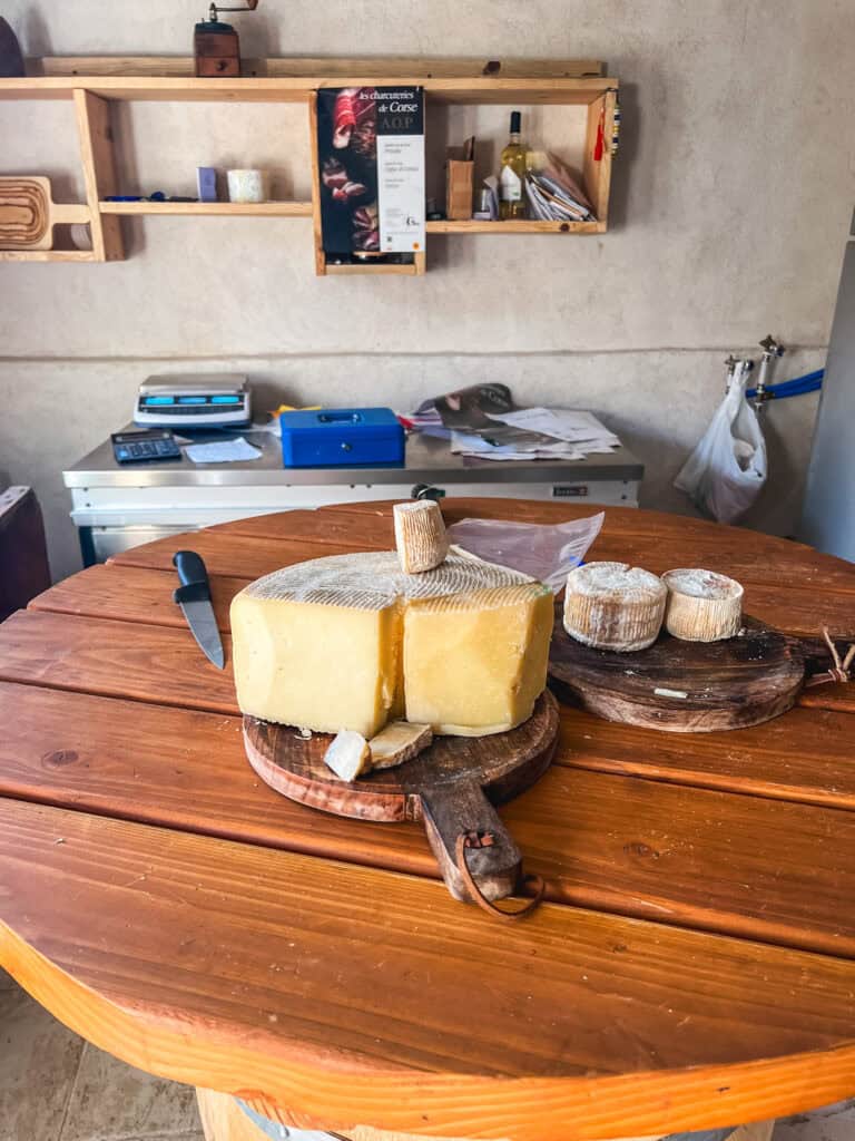 Wheel of Corsican sheep's milk cheese on a wooden board at a local fromagerie with AOP charcuterie sign — what to eat in Corsica local food