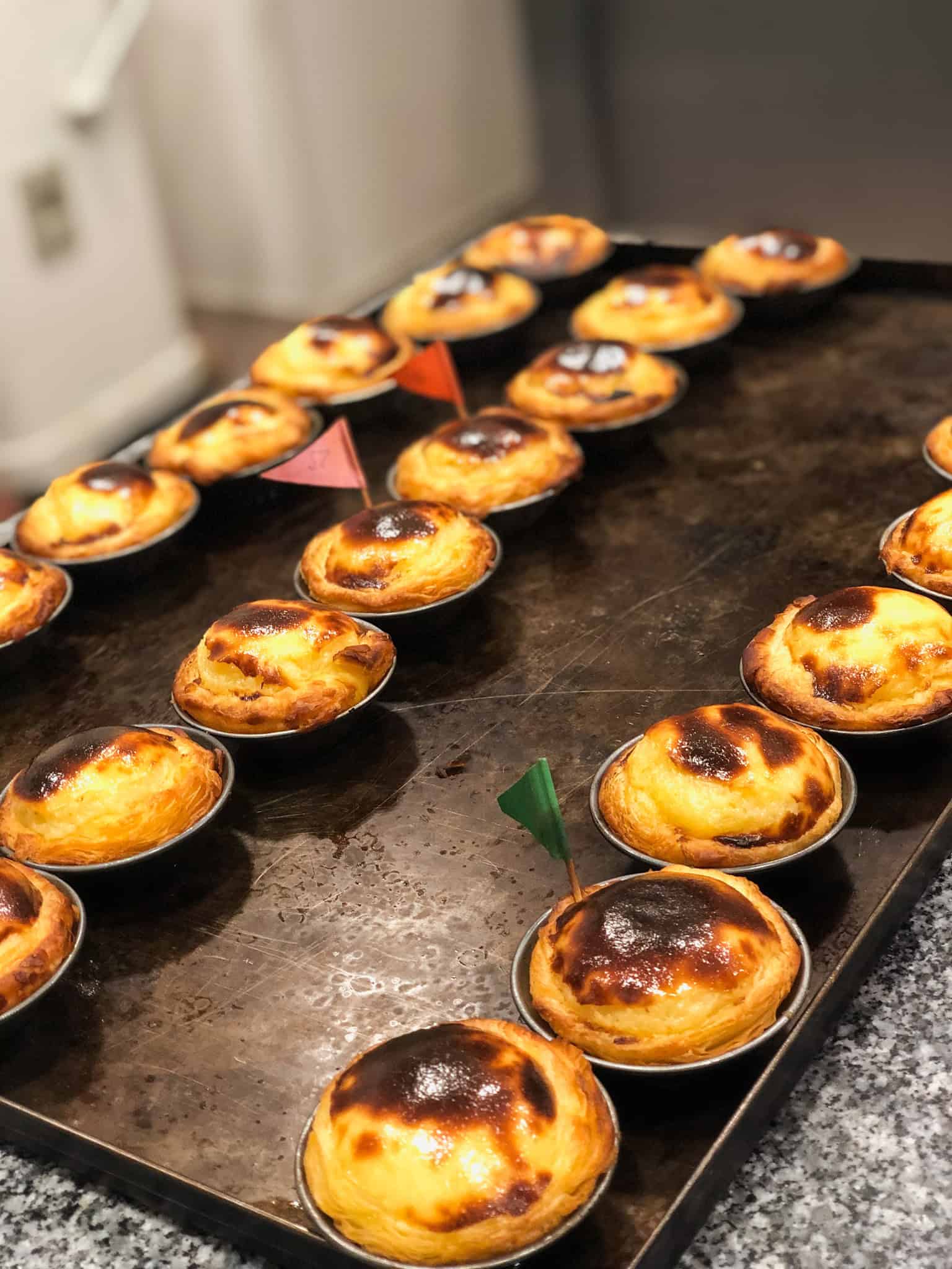 Freshly baked pastéis de nata on a baking tray at a Lisbon bakery — must-eat food in Lisbon Portugal on European summer vacations