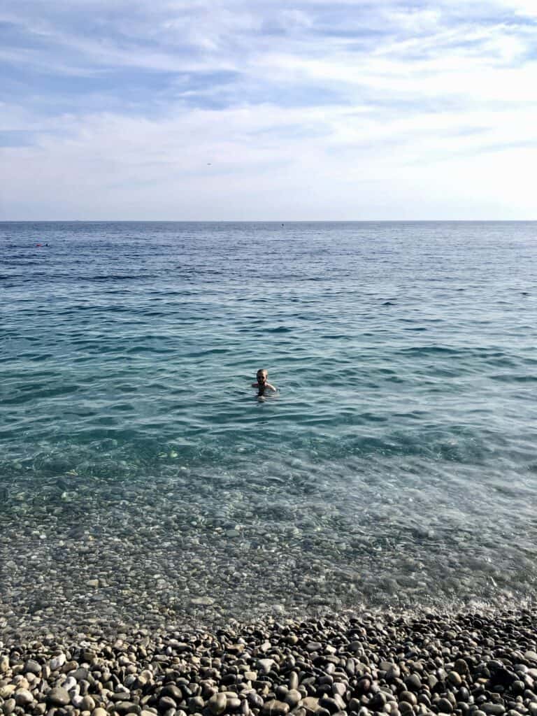 Person swimming in the clear turquoise water off the pebble beach in Nice, French Riviera — swimming in Nice France Côte d'Azur
