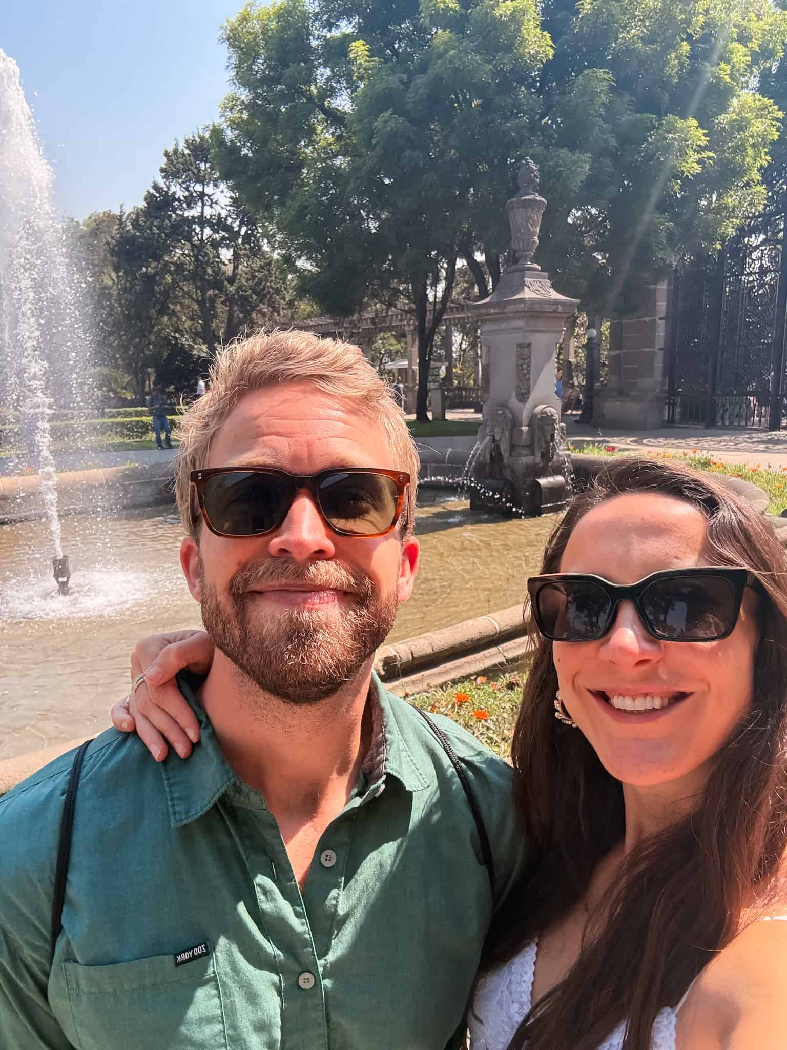 Couple smiling in front of a fountain and ornate iron gates in Chapultepec Park, Mexico City — is mexico safe to visit as a tourist destination for couples