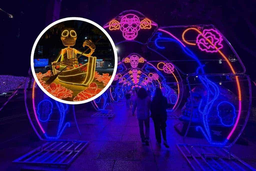 Neon light tunnel with glowing sugar skull arches on Paseo de la Reforma at night during Mexico City Day of the Dead celebrations, with an inset showing a skeleton rowing a boat surrounded by marigold lights