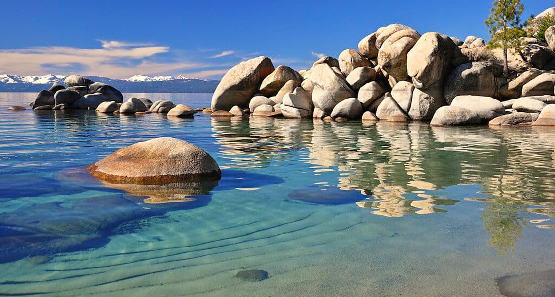 Clear turquoise water and smooth granite boulders at Chimney Beach on Lake Tahoe's east shore, with snow-capped peaks visible across the lake