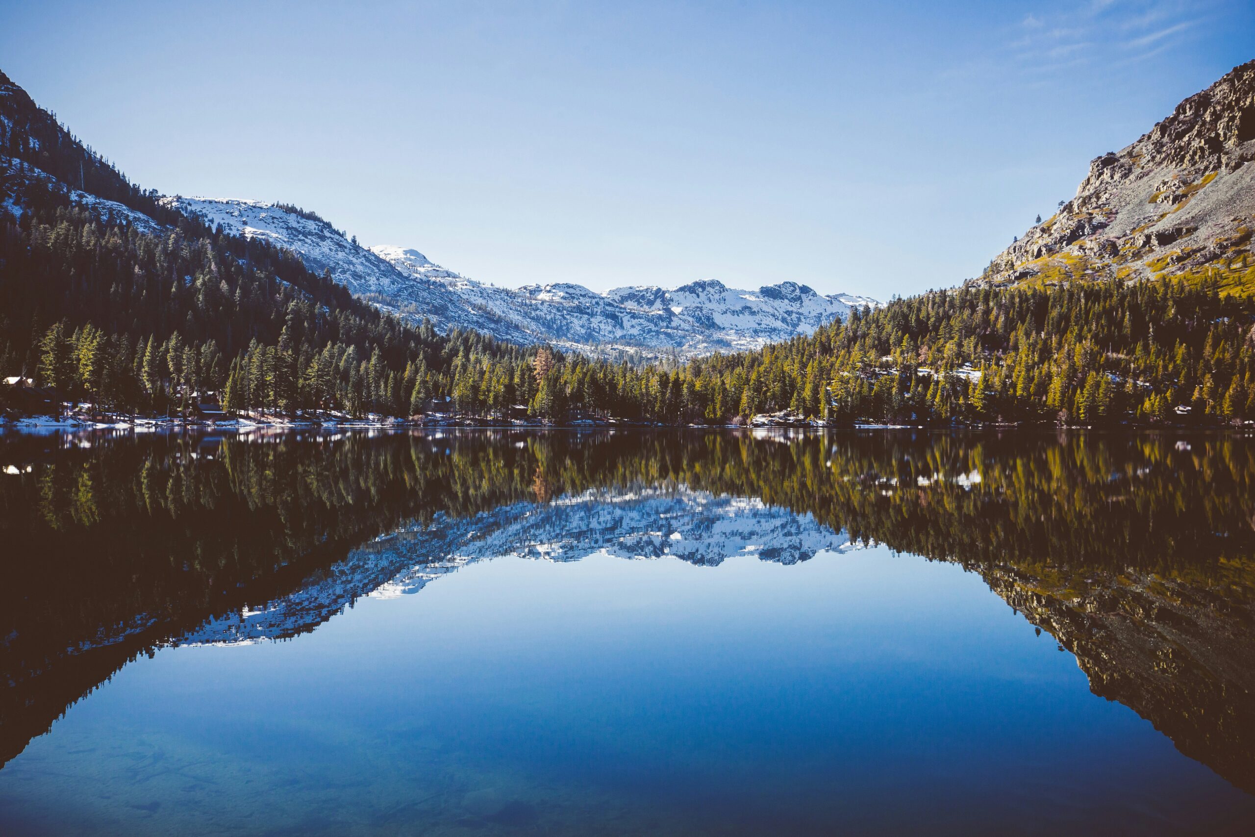 Mirror-still reflection of snow-dusted Sierra Nevada peaks and pine forest in Fallen Leaf Lake near South Lake Tahoe
