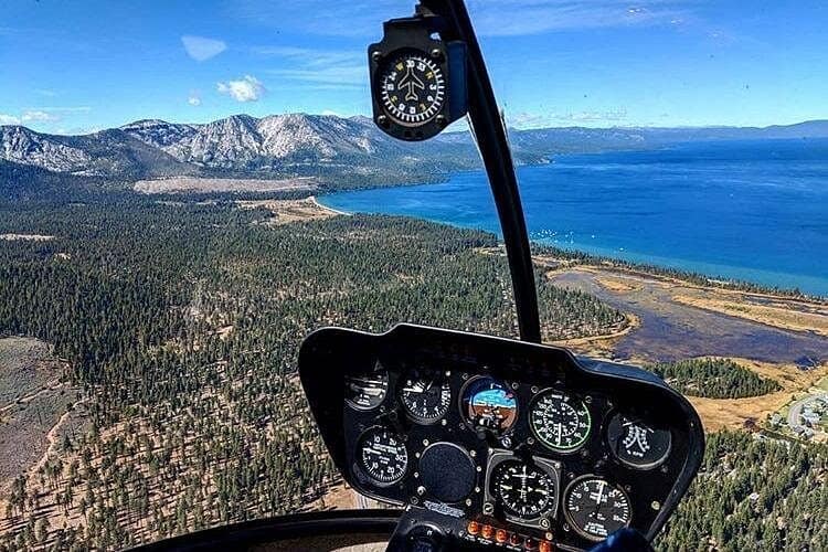 Helicopter cockpit view over South Lake Tahoe showing the blue shoreline, pine forest, and Sierra Nevada mountains during an aerial tour