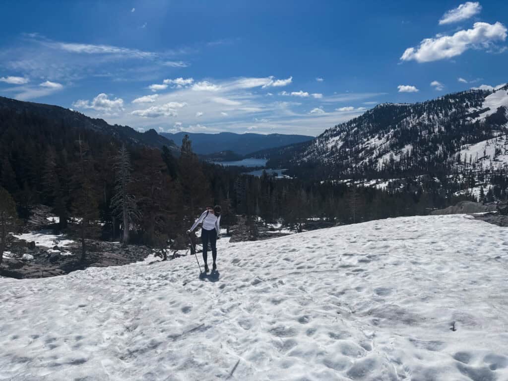 Hiker using trekking poles to cross a snow-covered slope above a mountain lake in the Sierra Nevada, one of the best things to do in Tahoe in spring