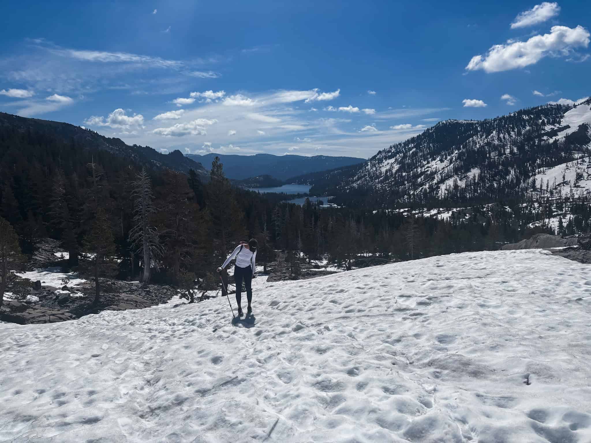 Hiker using trekking poles to cross a snow-covered slope above a mountain lake in the Sierra Nevada, one of the best things to do in Tahoe in spring