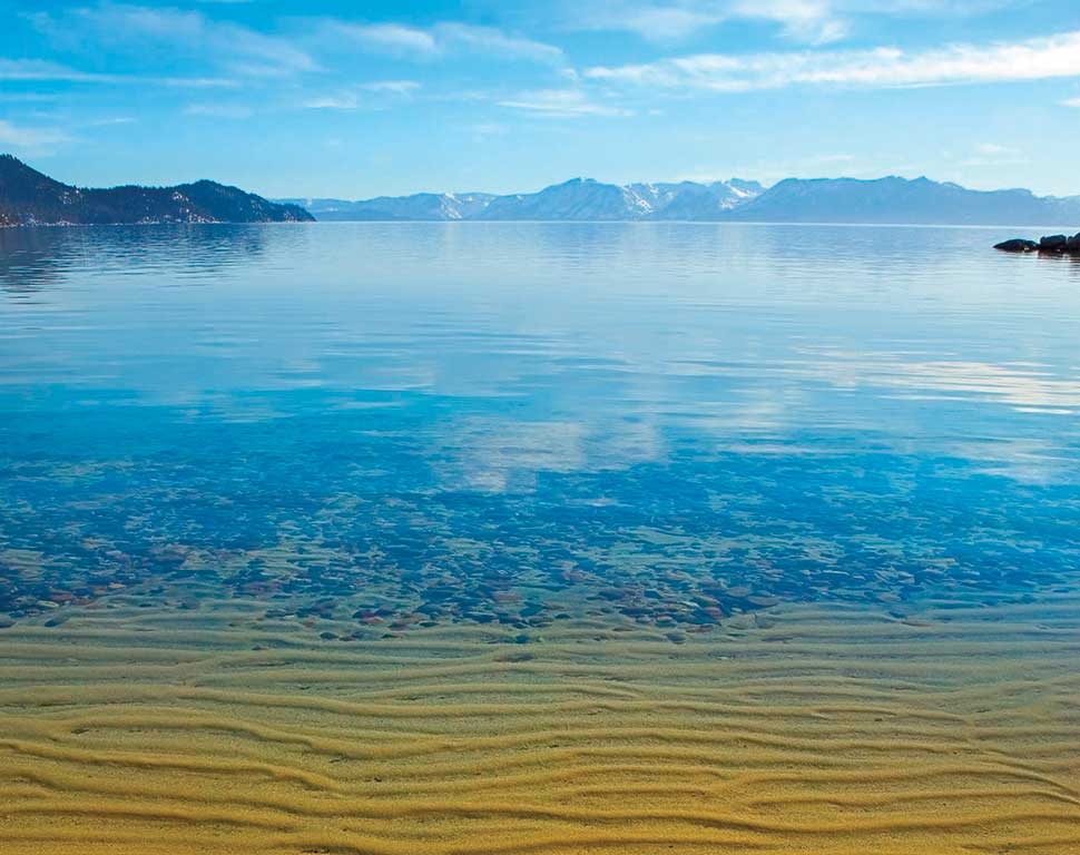 Secluded sandy beach at Secret Cove on Lake Tahoe's Nevada side with deep blue water and granite boulders scattered along the shoreline