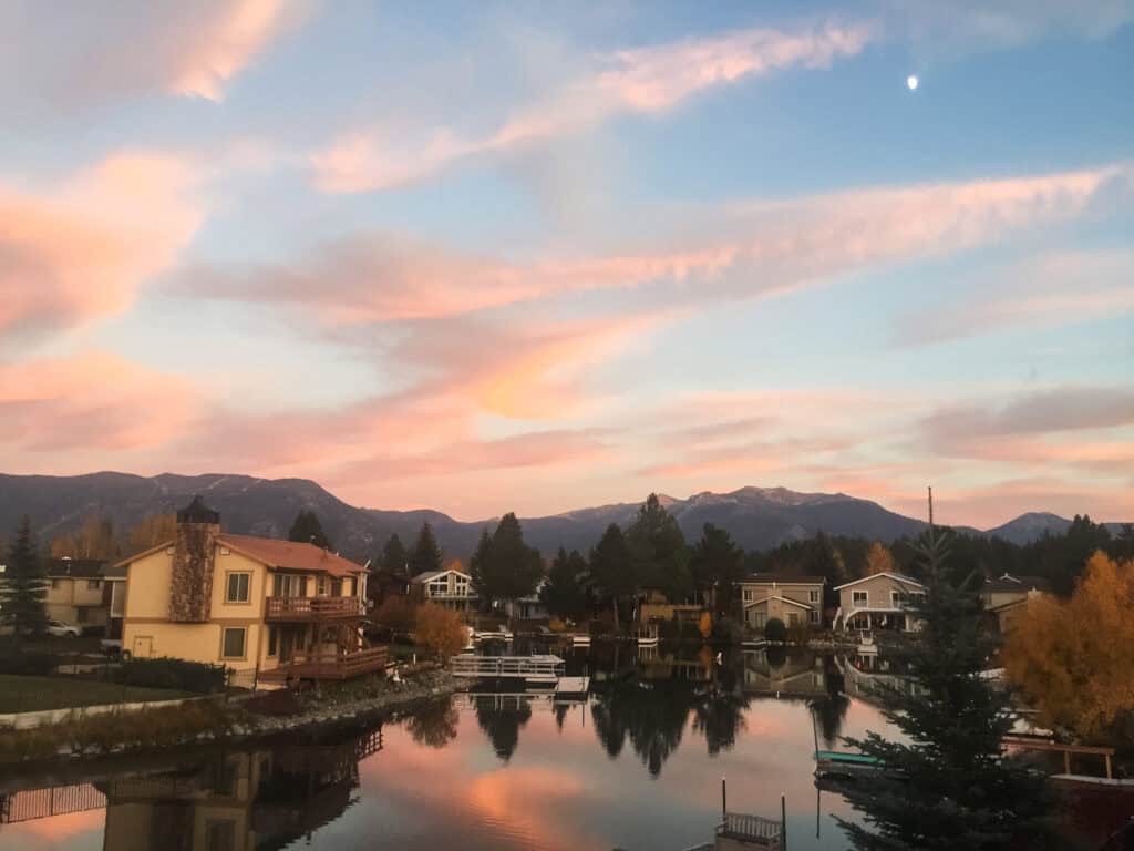 Pink and peach sunset reflecting in a South Lake Tahoe canal with lakefront homes, pine trees, and the Sierra Nevada glowing behind
