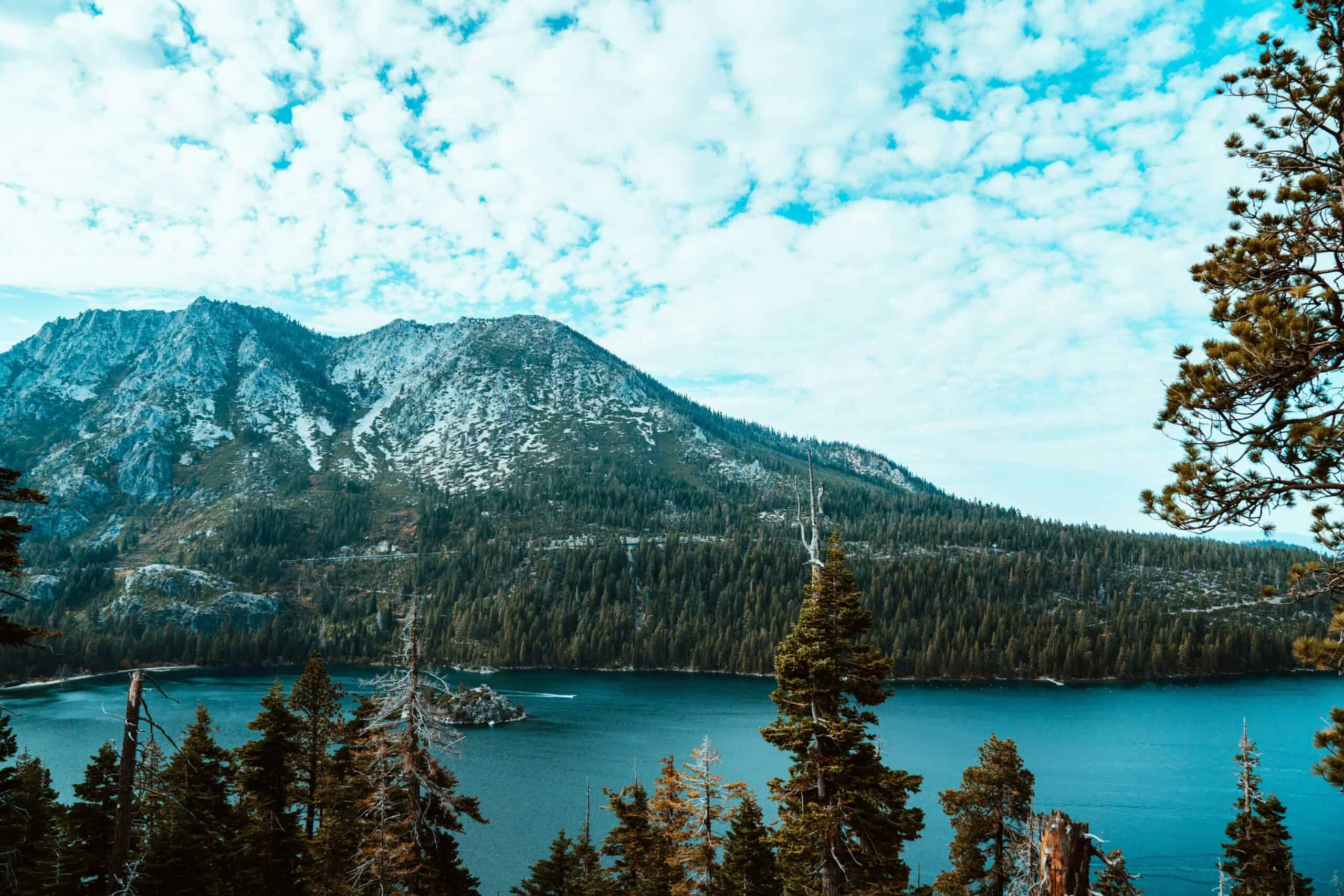 Wide view of Emerald Bay from the Mount Tallac area with Fannette Island visible in the blue-green water and snow-streaked peaks rising behind