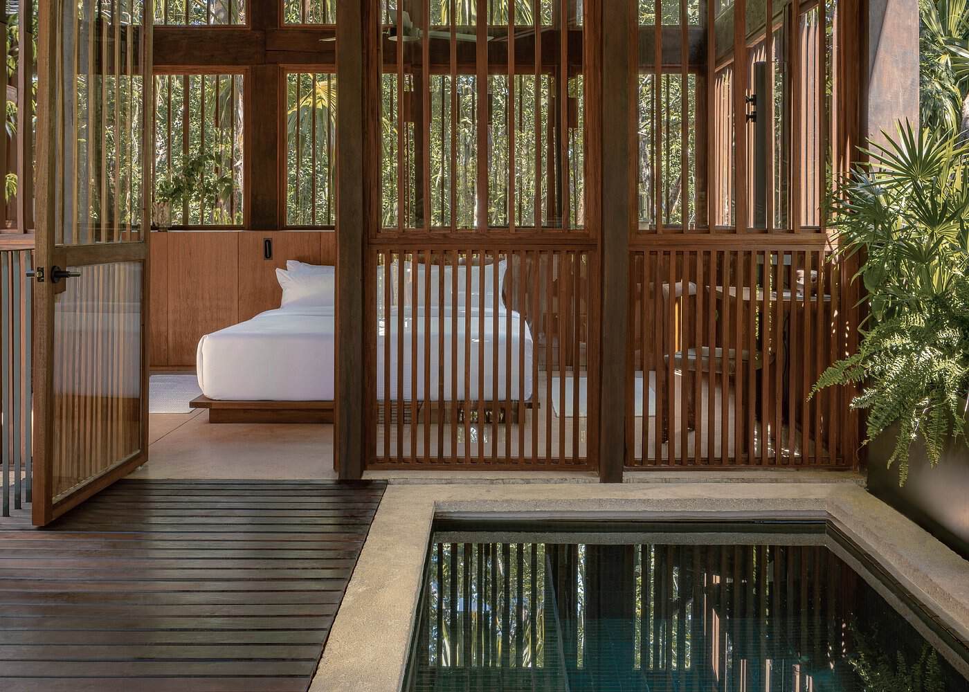 Open-air jungle villa room at Boca de Agua Bacalar with slatted wood walls, white platform bed, and a private plunge pool surrounded by tropical foliage