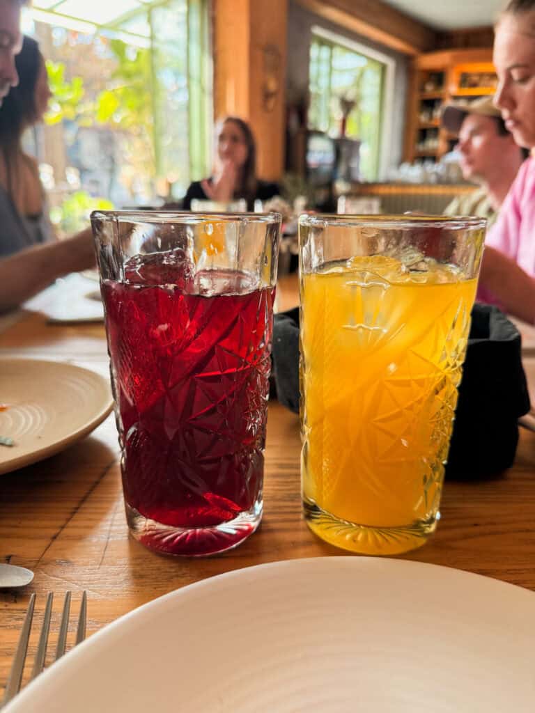 Hibiscus agua fresca and fresh orange juice in cut glass tumblers on a wooden table during a Mexico City food tour
