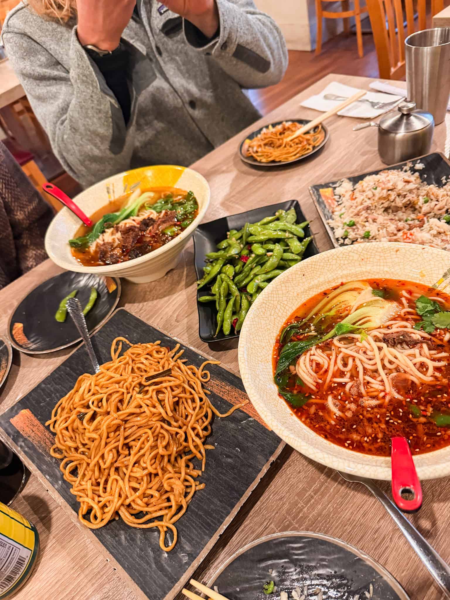 Table spread of spicy noodle soup, lo mein, edamame, and fried rice at an Asian restaurant in South Lake Tahoe