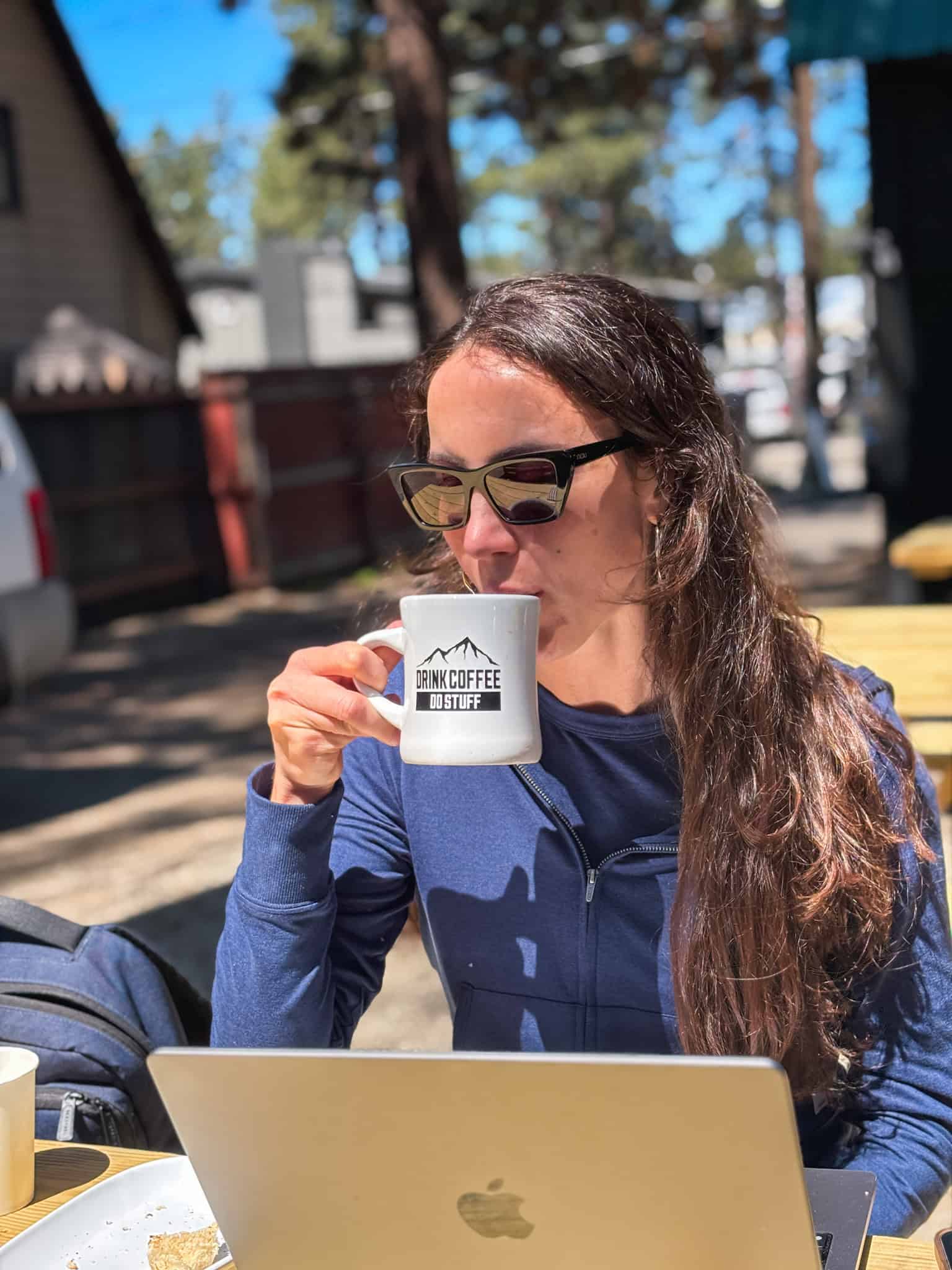 Woman drinking coffee from a "Drink Coffee Do Stuff" mug at an outdoor café patio in South Lake Tahoe