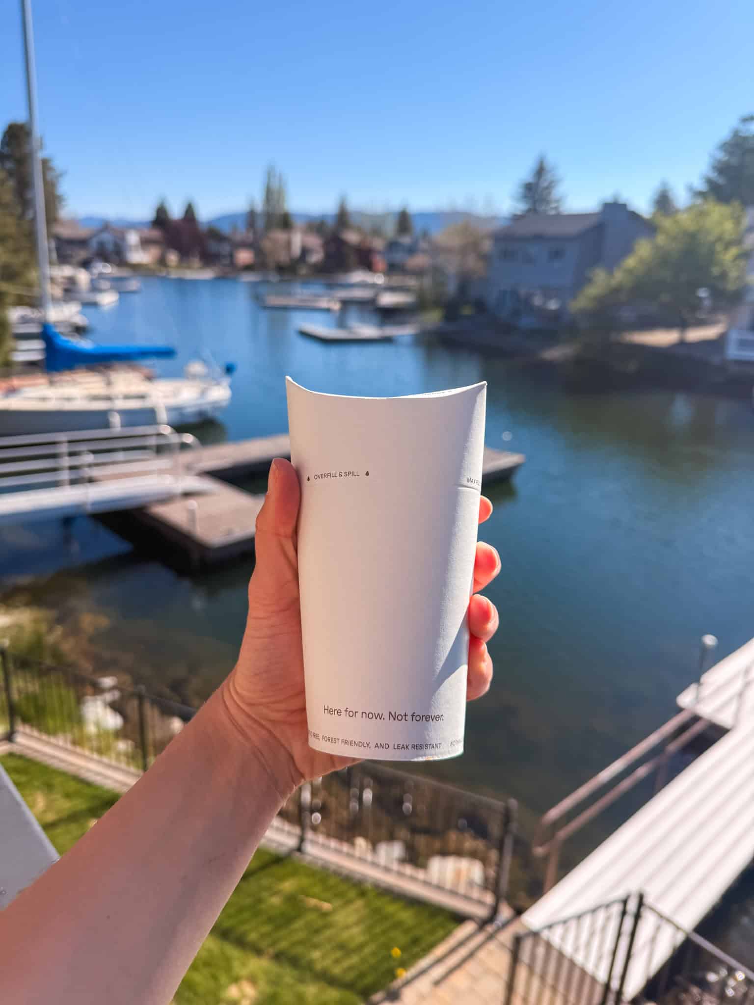 Hand holding a to-go coffee cup overlooking a marina with docks and sailboats in South Lake Tahoe