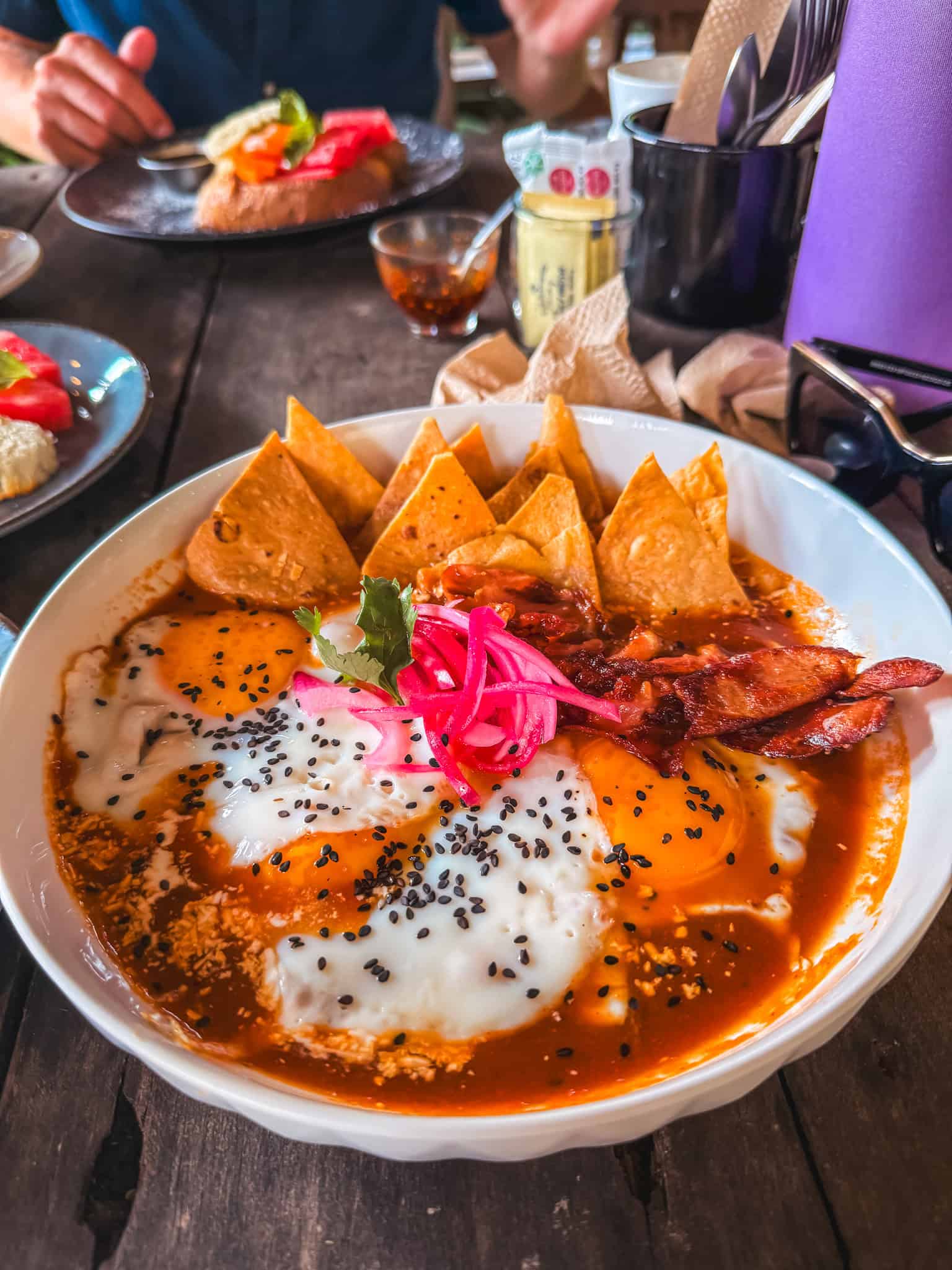 Chilaquiles with tortilla chips, fried eggs, bacon and pickled onions at a restaurant in Bacalar, great for breakfast near the lagoon