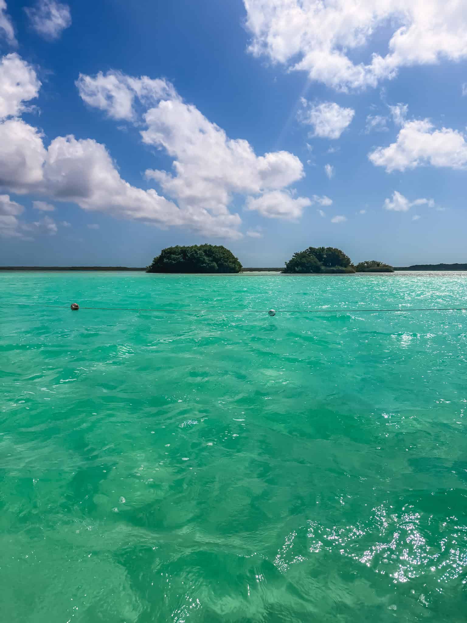 Two small mangrove bird islands rising from the glassy turquoise waters of Laguna Bacalar, seen from a boat tour on the lake