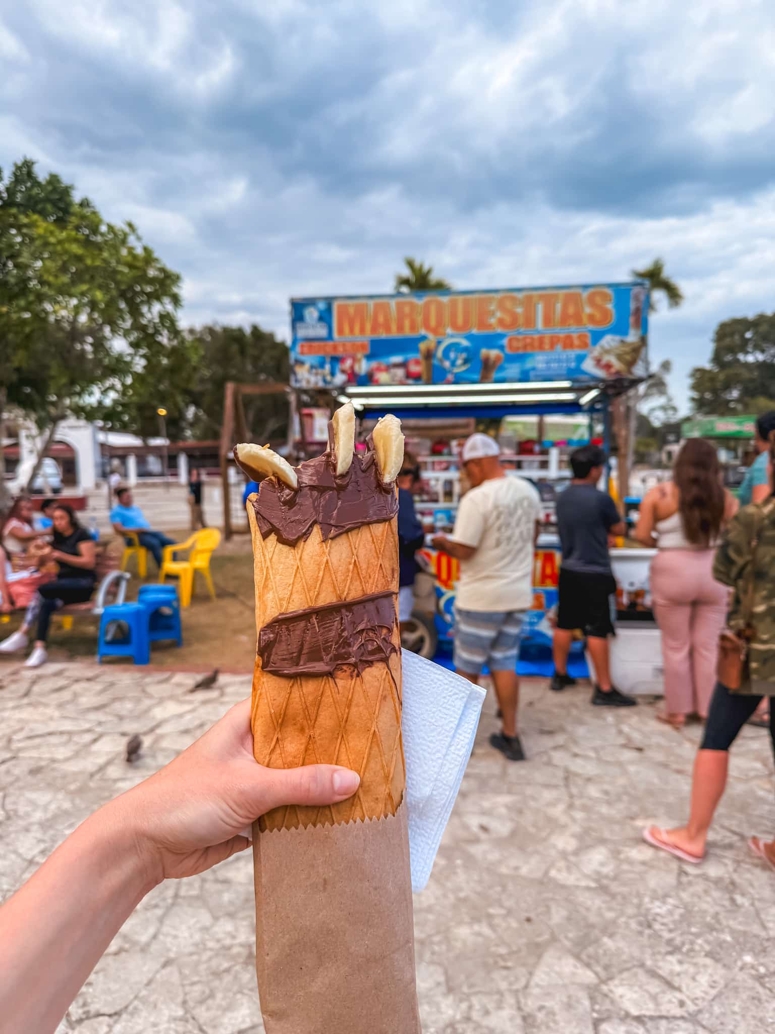 Hand holding a chocolate banana marquesita from a street food cart, a classic Bacalar activity and taste of local Mexican street food