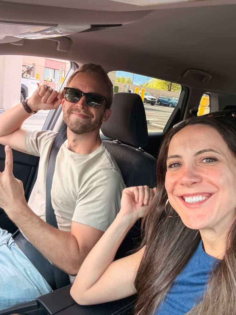 Two people laughing in the front seat of a rental car, driving to Lake Tahoe from Reno airport