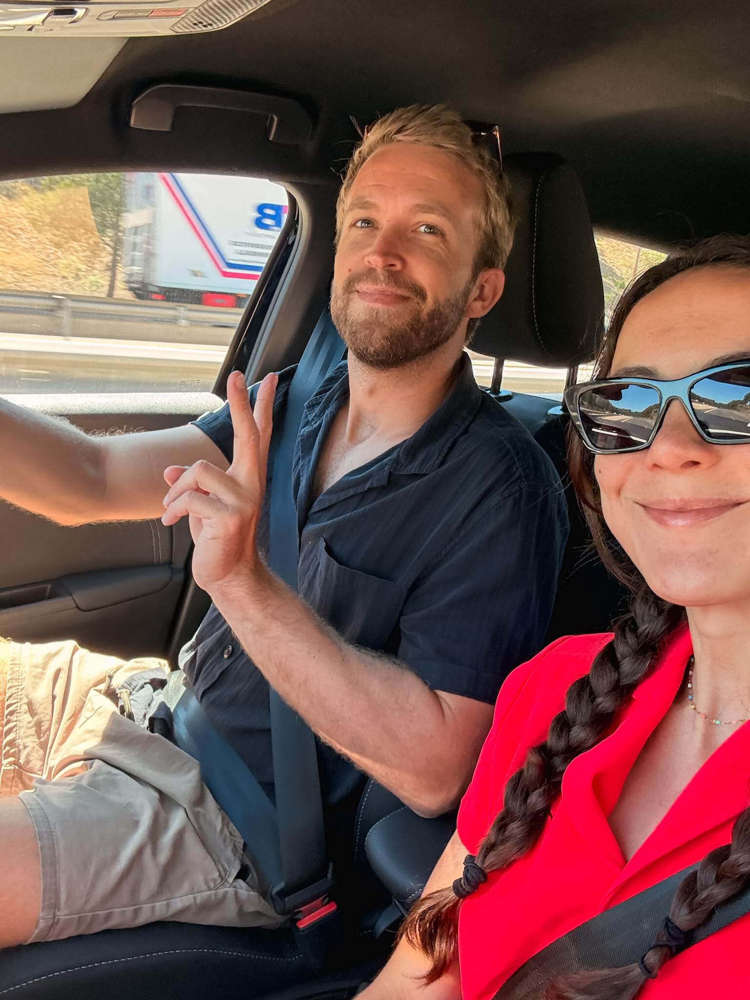 Couple giving a peace sign from inside their car on the motorway, mid road trip in Mallorca.