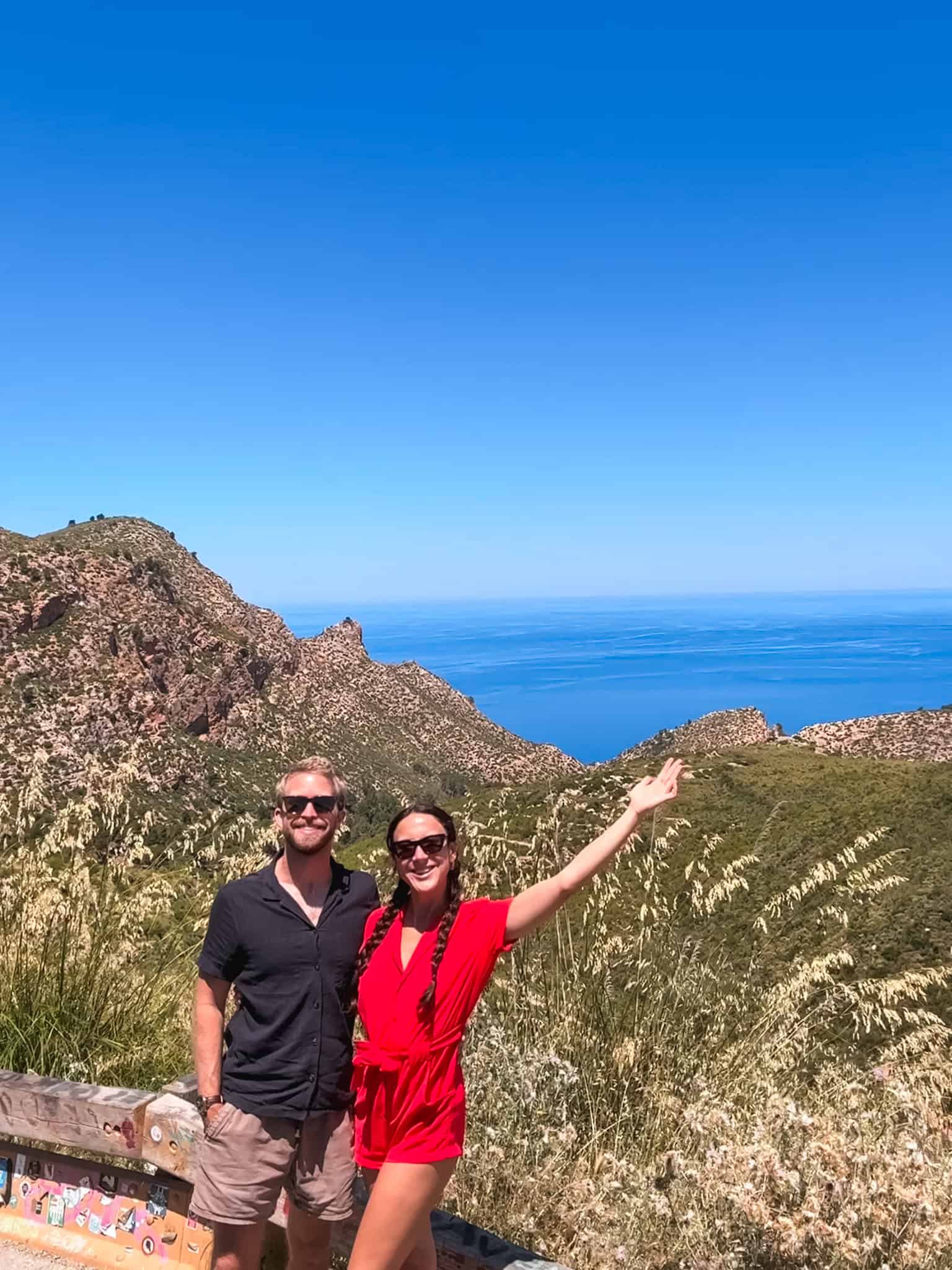 Couple posing at a mountain viewpoint overlooking the coastline, one of the best stops when driving in Mallorca.