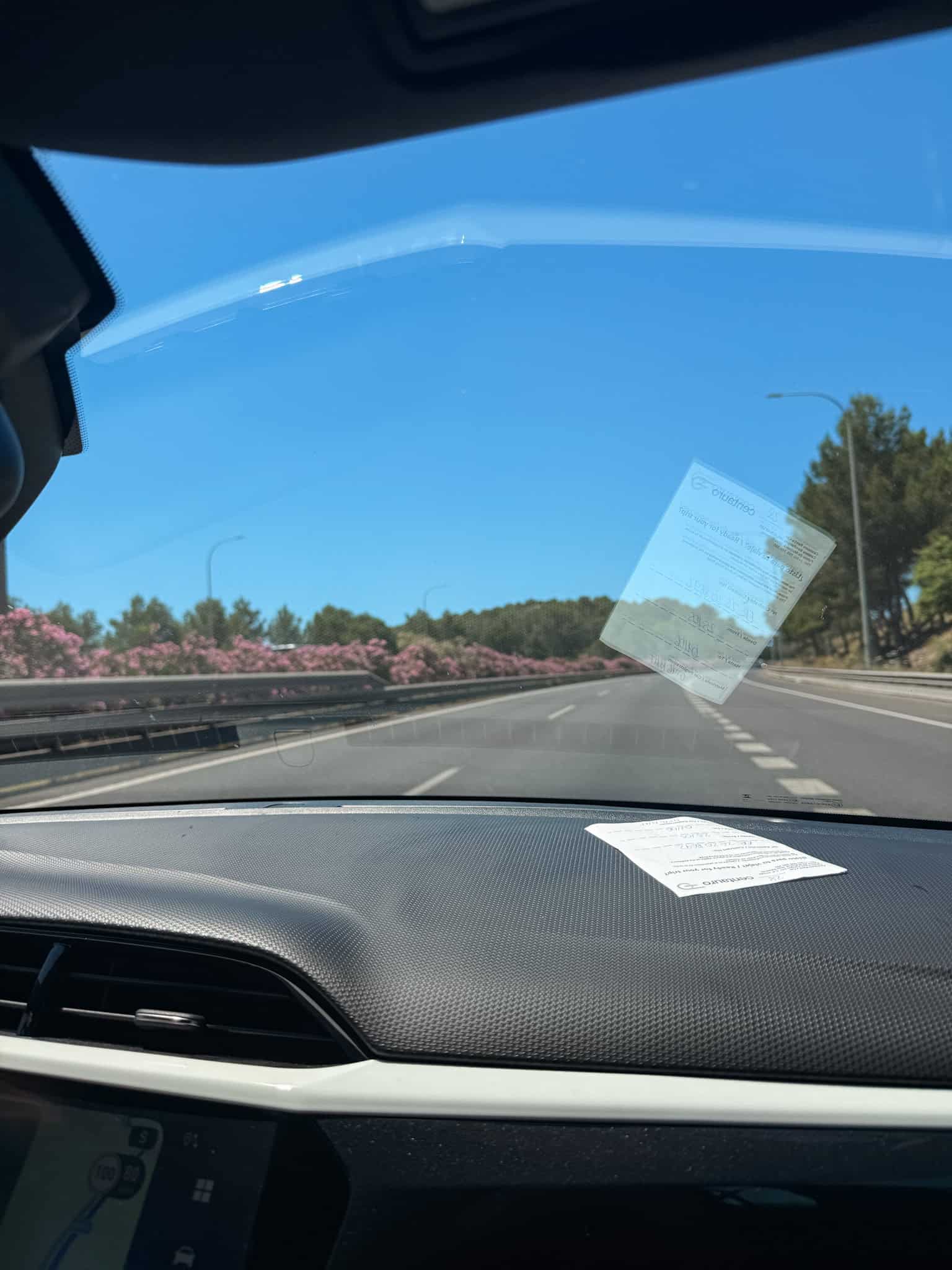 Rental agreement papers on the car dashboard with a view of the highway and pink oleander bushes ahead.
