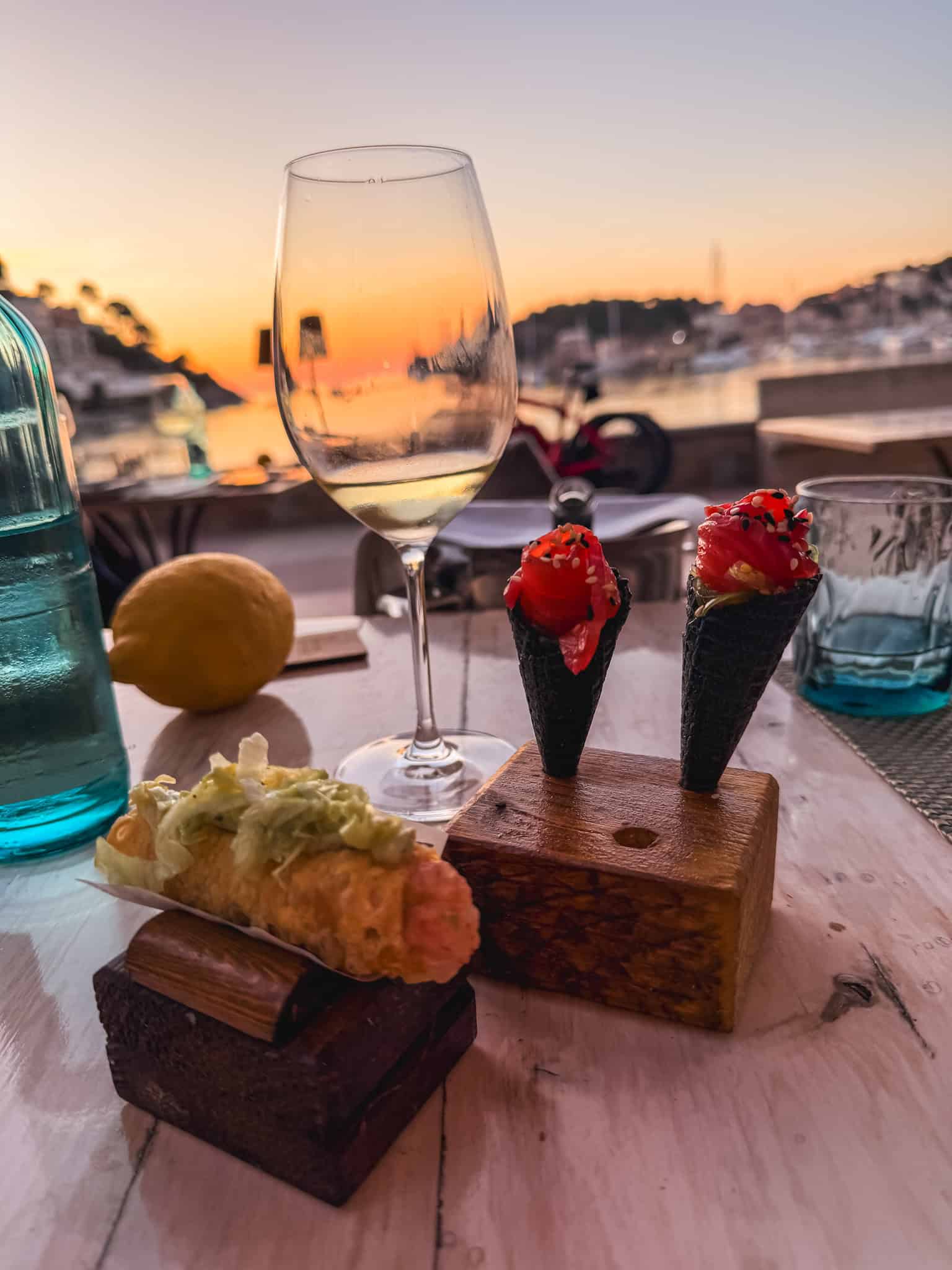 Sushi appetizers and wine with sunset views over Port de Sóller harbor