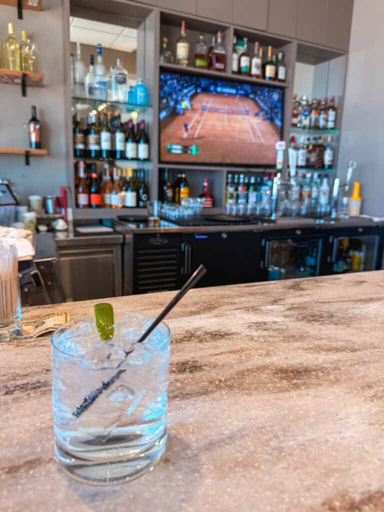 Full bar with stocked liquor shelves and a gin and tonic on the marble counter at the Escape Lounge, Reno airport