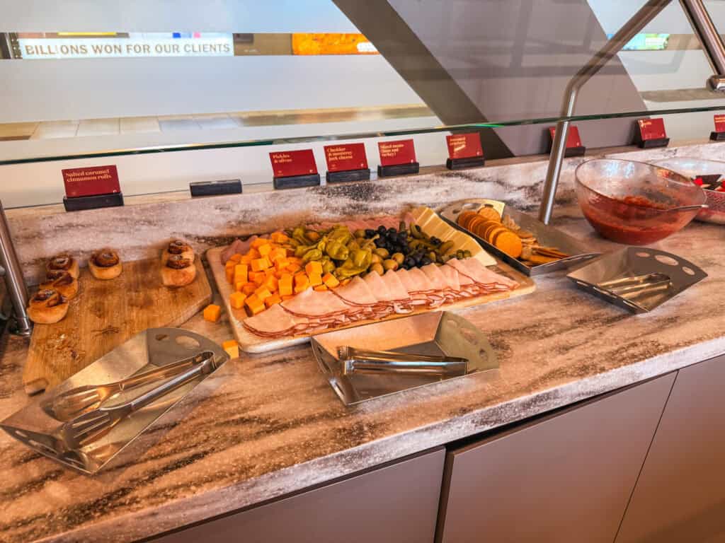 Charcuterie board with sliced turkey, cheddar, pickles, and olives at the Escape Lounge Reno airport, with salted caramel cinnamon rolls on the side