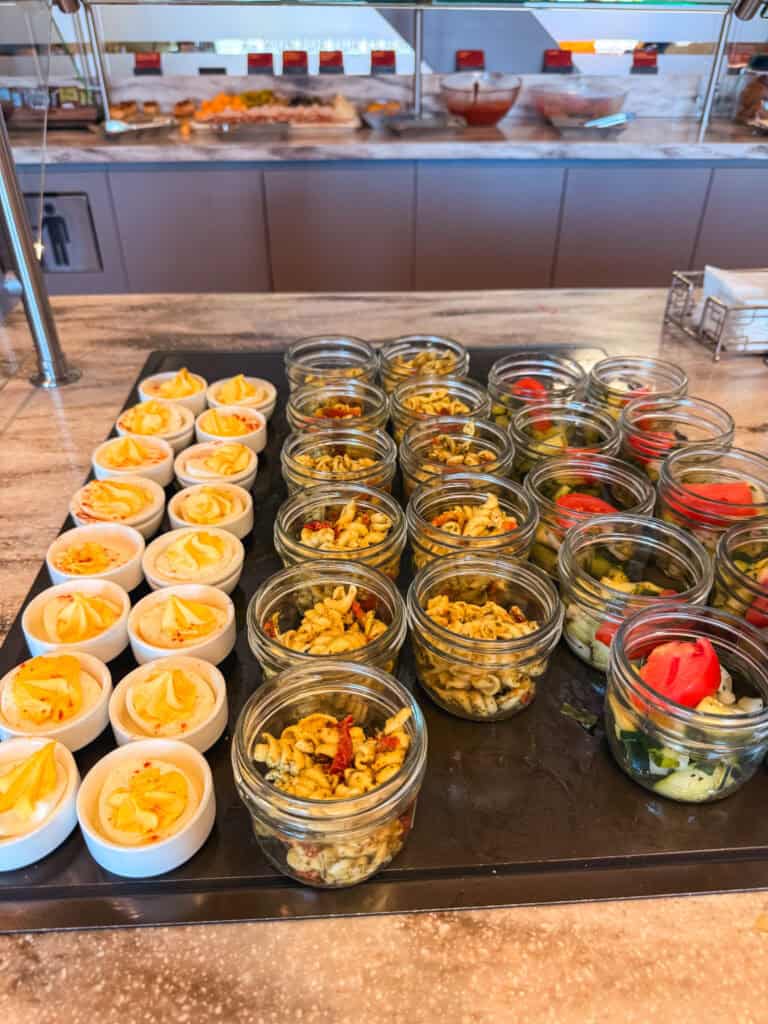 Reno Tahoe airport lounge review food spread showing deviled eggs, pasta salad jars, and chopped salad cups on the self-serve buffet counter