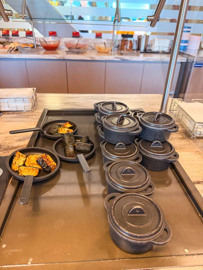 Hot food station at the Reno Tahoe airport lounge review featuring mini cast iron pots and roasted vegetable skillets on the buffet