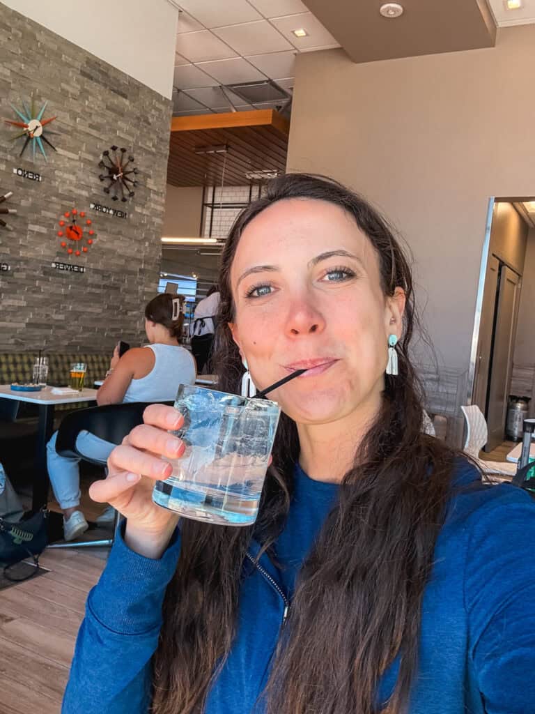 Woman sipping a cocktail inside the Escape Lounge at Reno-Tahoe International Airport with mid-century clocks on the stone accent wall behind her