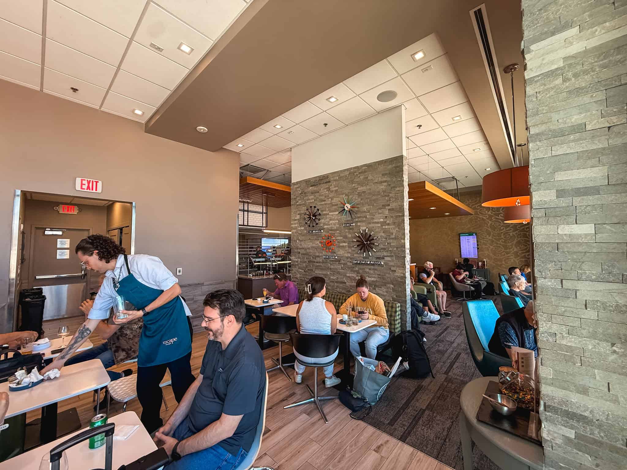 Interior seating area of the Escape Lounge at Reno-Tahoe airport with a staff member serving guests at dining tables alongside a lounge seating section