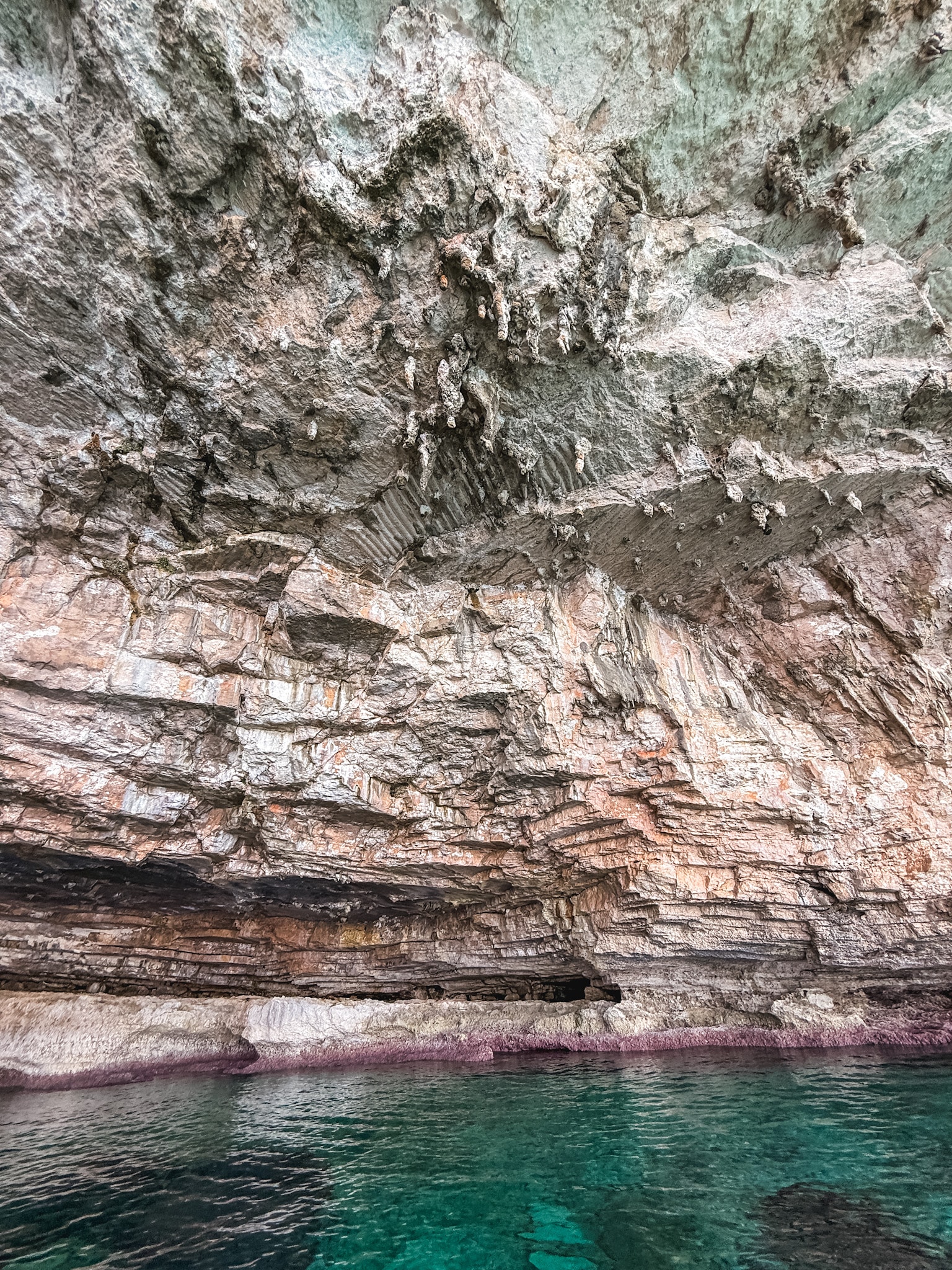 Layered limestone cave ceiling with pink algae staining the rock above deep turquoise water on a Mallorca boat tour.
