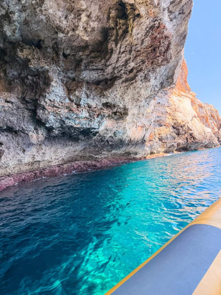 Sunlit orange cave walls rising above clear blue water, part of the sea caves explored on Mallorca boat tours.