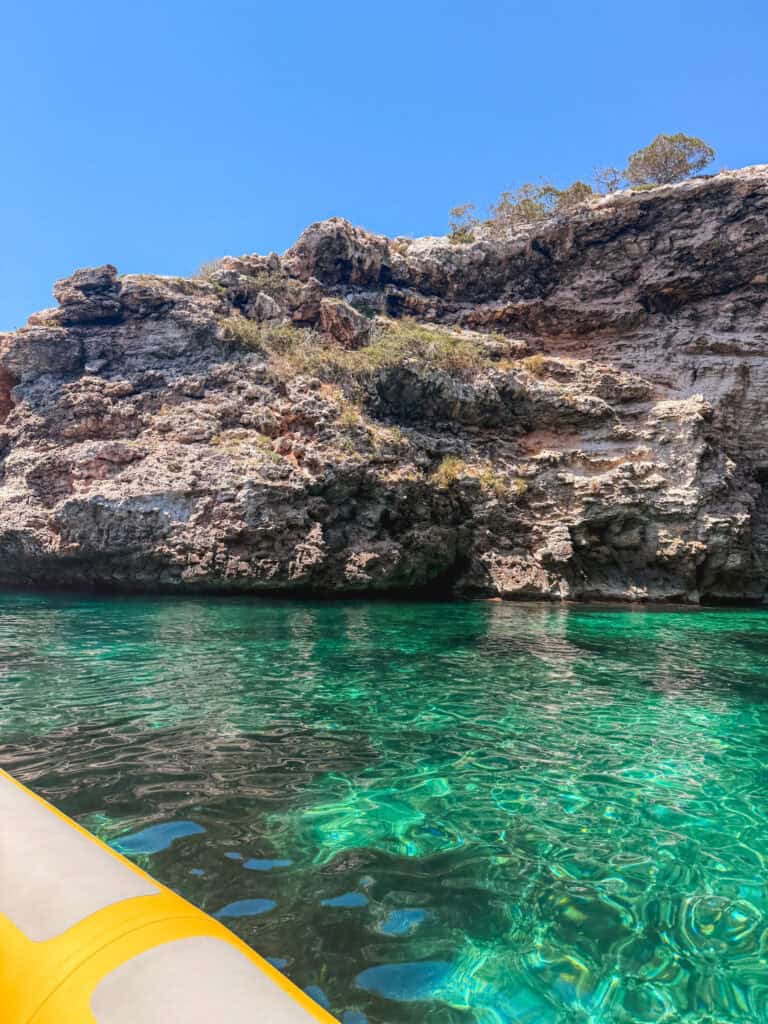 View from the boat showing emerald green water meeting rugged limestone rock along the Mallorca coastline.