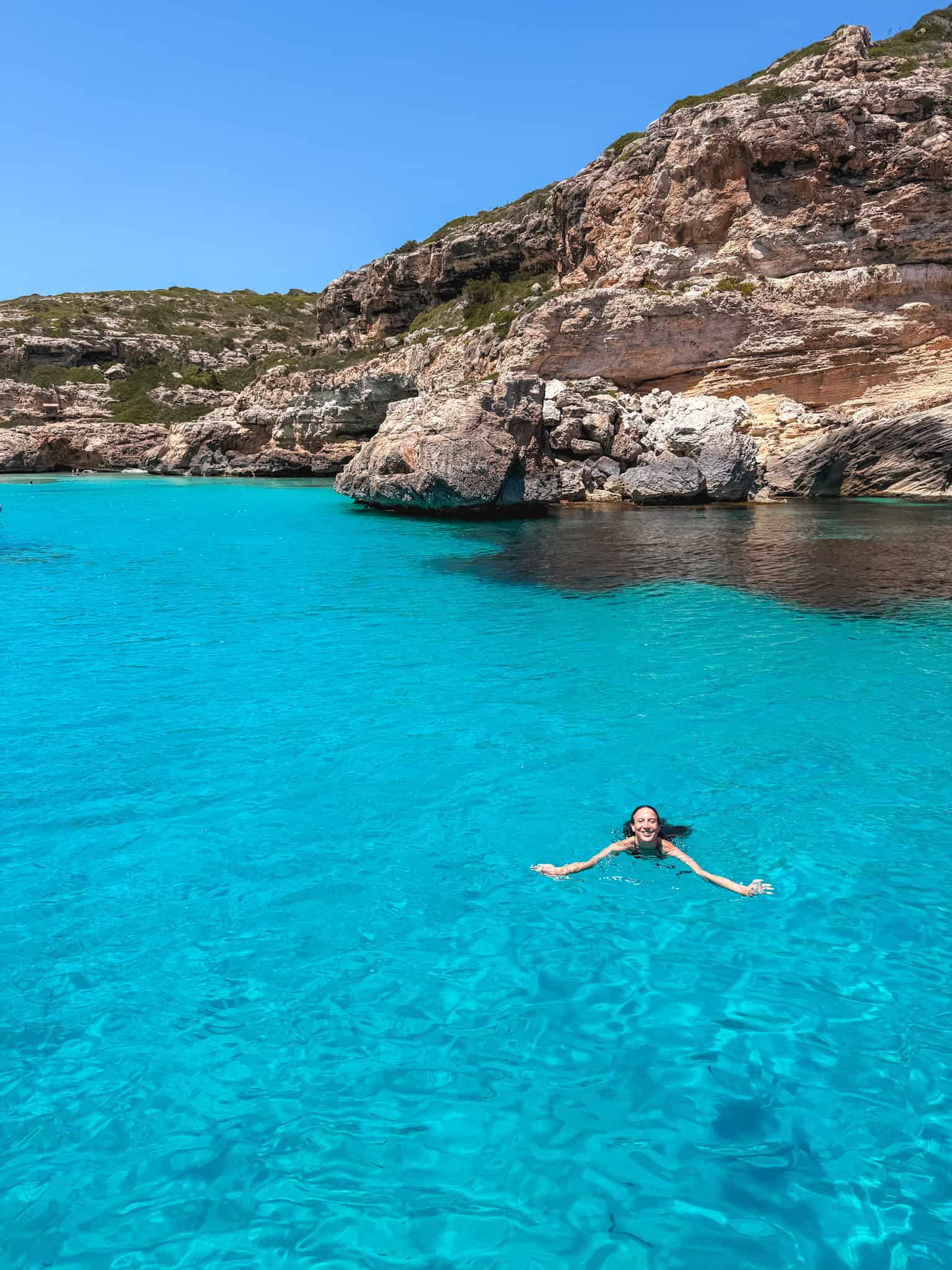 woman swimming in clear turquoise water during a stop on the boat tour, cliffs rising behind.
