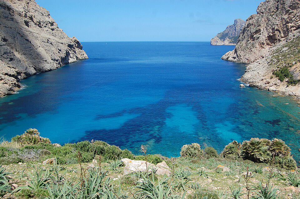 Deep blue cove at Cala Boquer near Port de Pollença, steep limestone cliffs framing the calm water