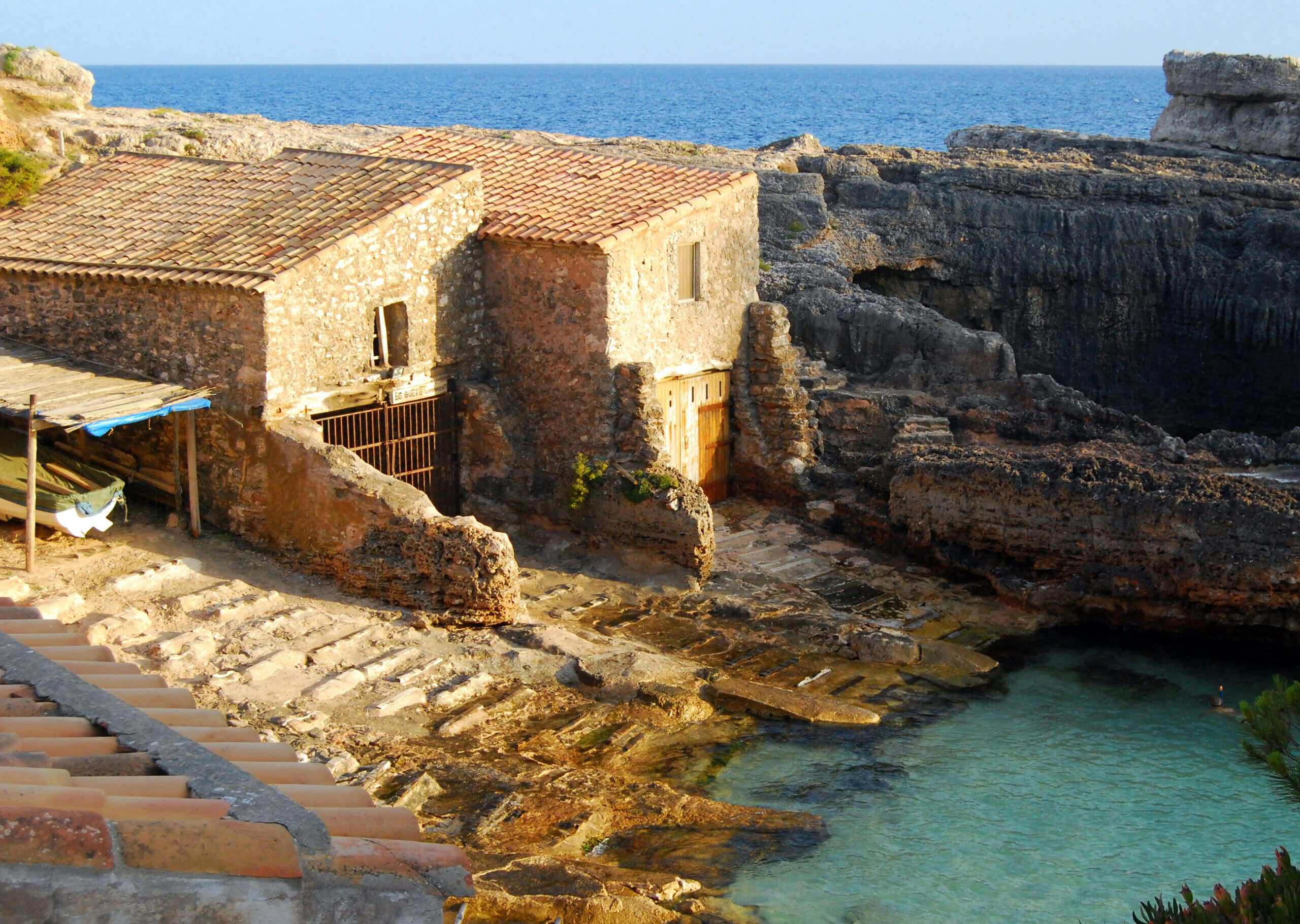 Traditional stone boathouses at Cala s'Almunia, clear shallow water meeting weathered coastal rock