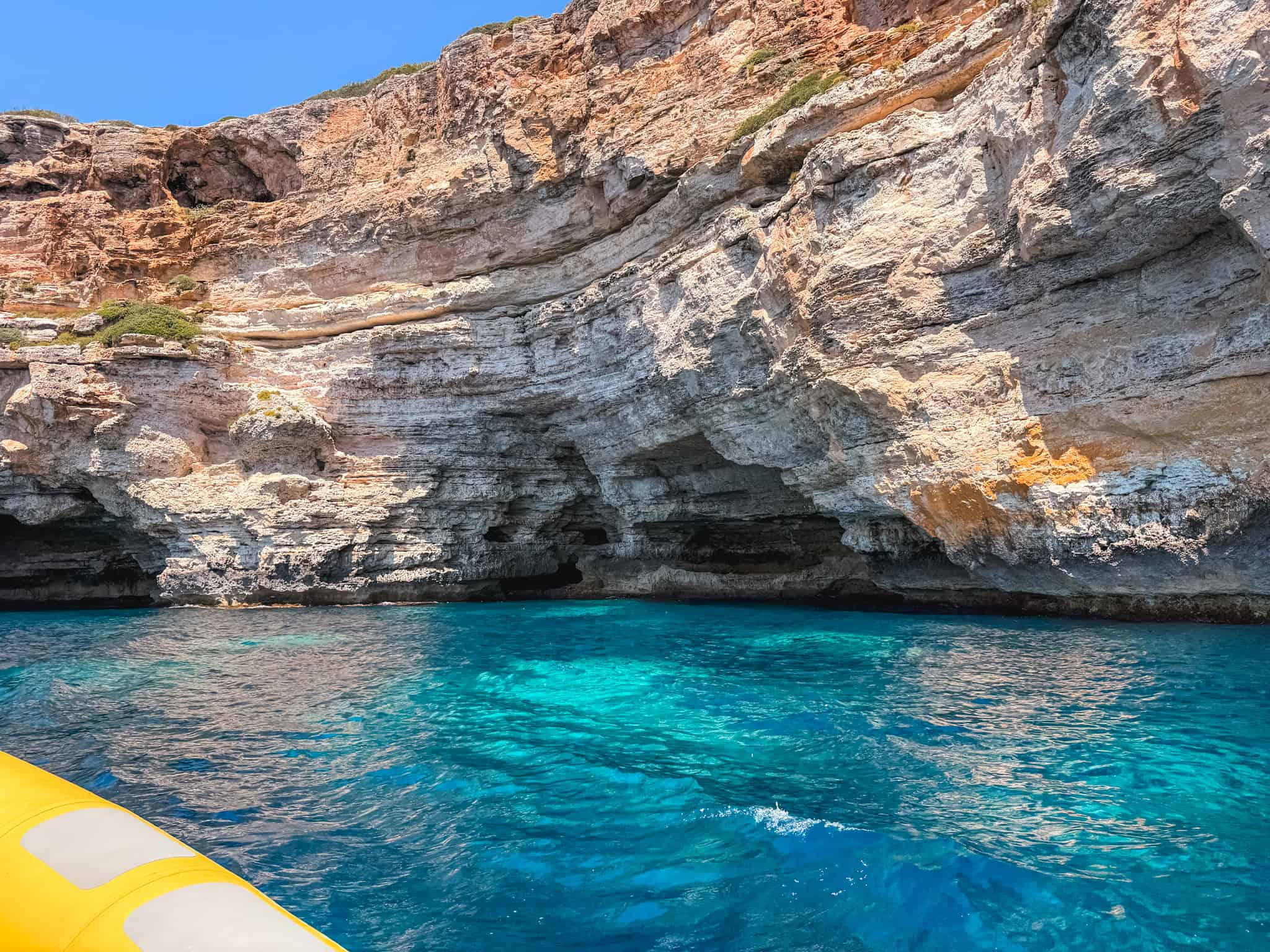 View from a boat entering a sea cave near one of the best beaches in Mallorca, turquoise water beneath golden cliffs