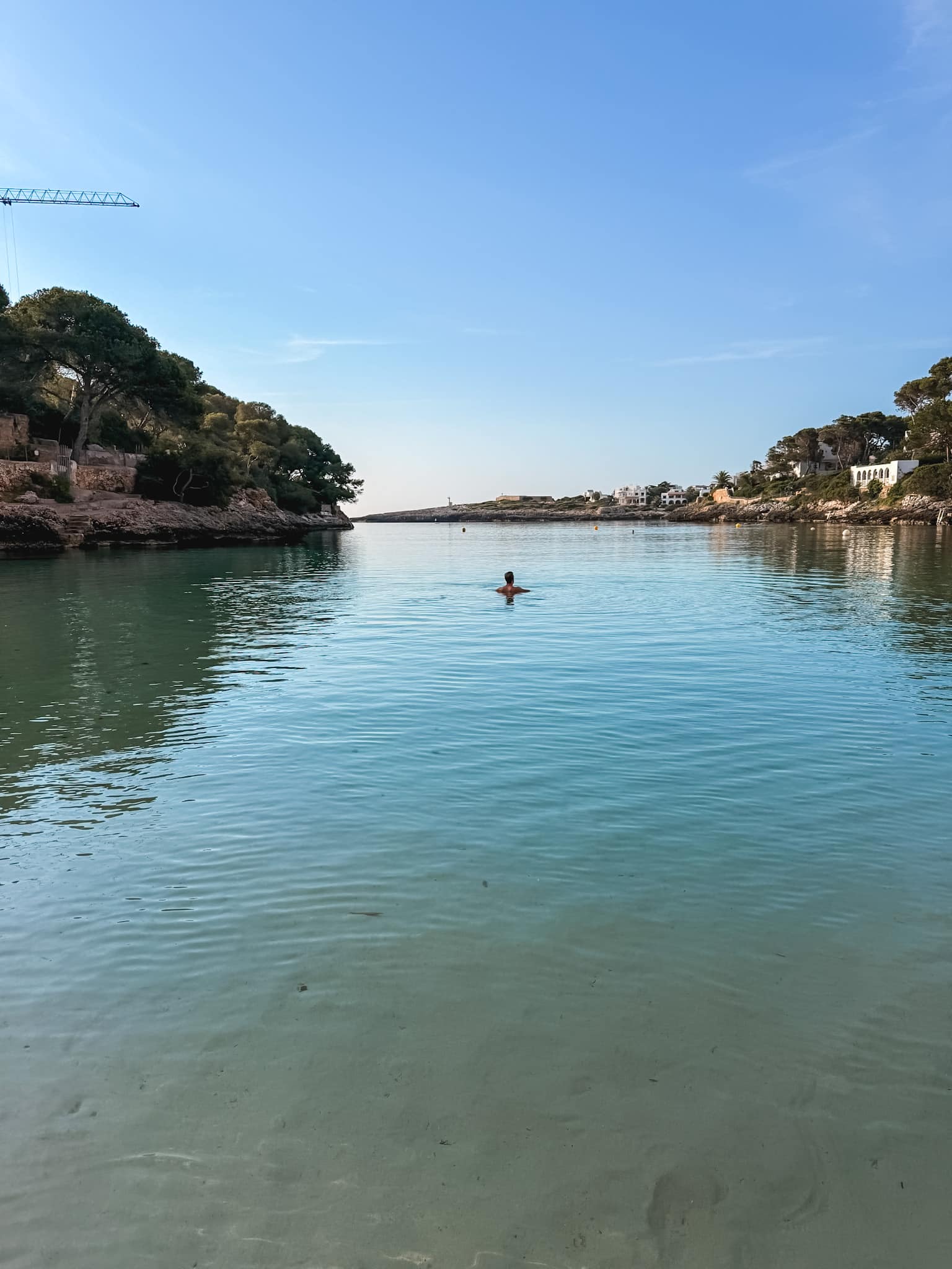 Calm clear water in a quiet Mallorca cove at sunrise, a swimmer floating near the shoreline